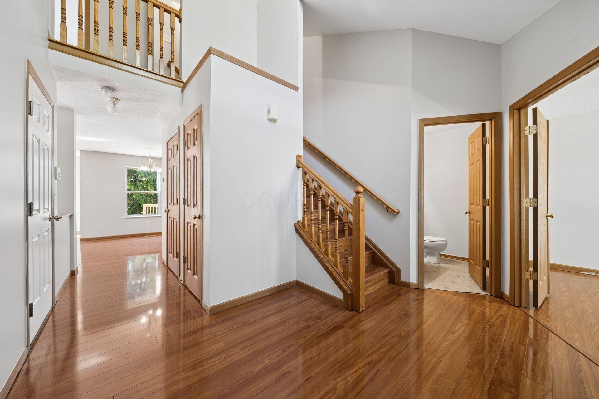 Two-story entry hall with polished hardwood floors, wooden staircase, and open doorways.