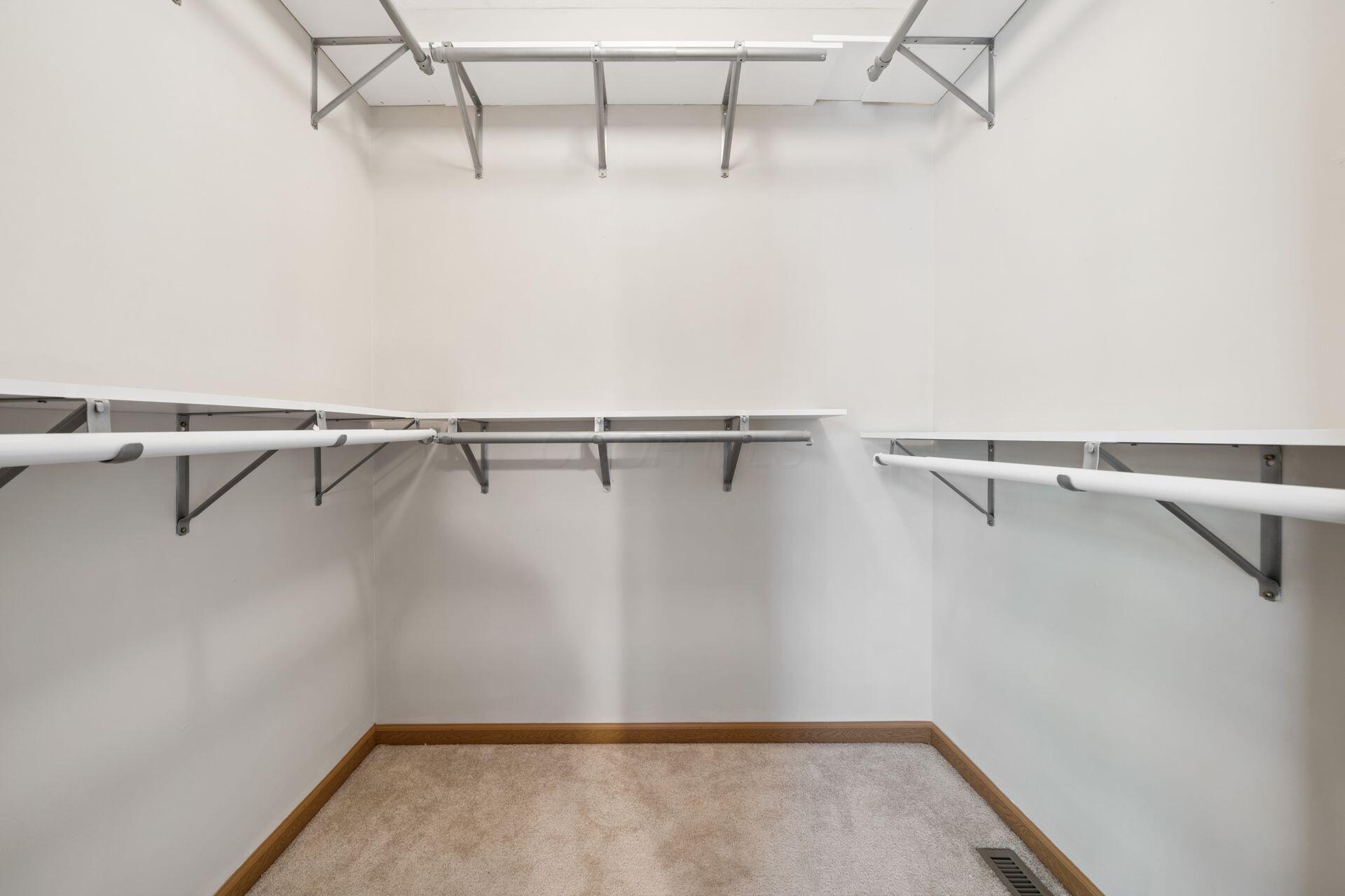 Empty walk-in closet with carpet and clothes rods and shelves along three walls.
