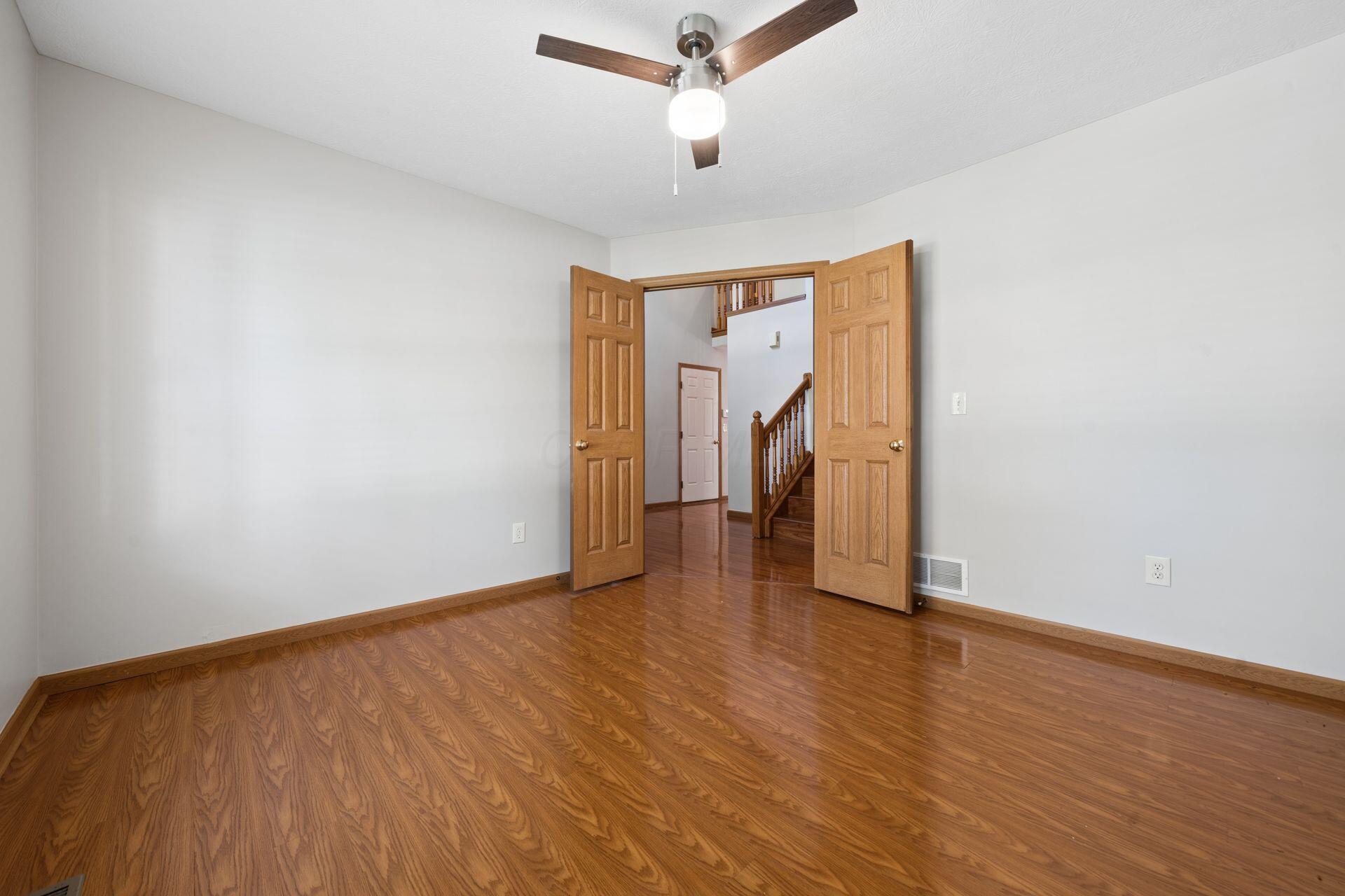 Empty room with hardwood floors, a wood ceiling fan, and double doors opening to a staircase.