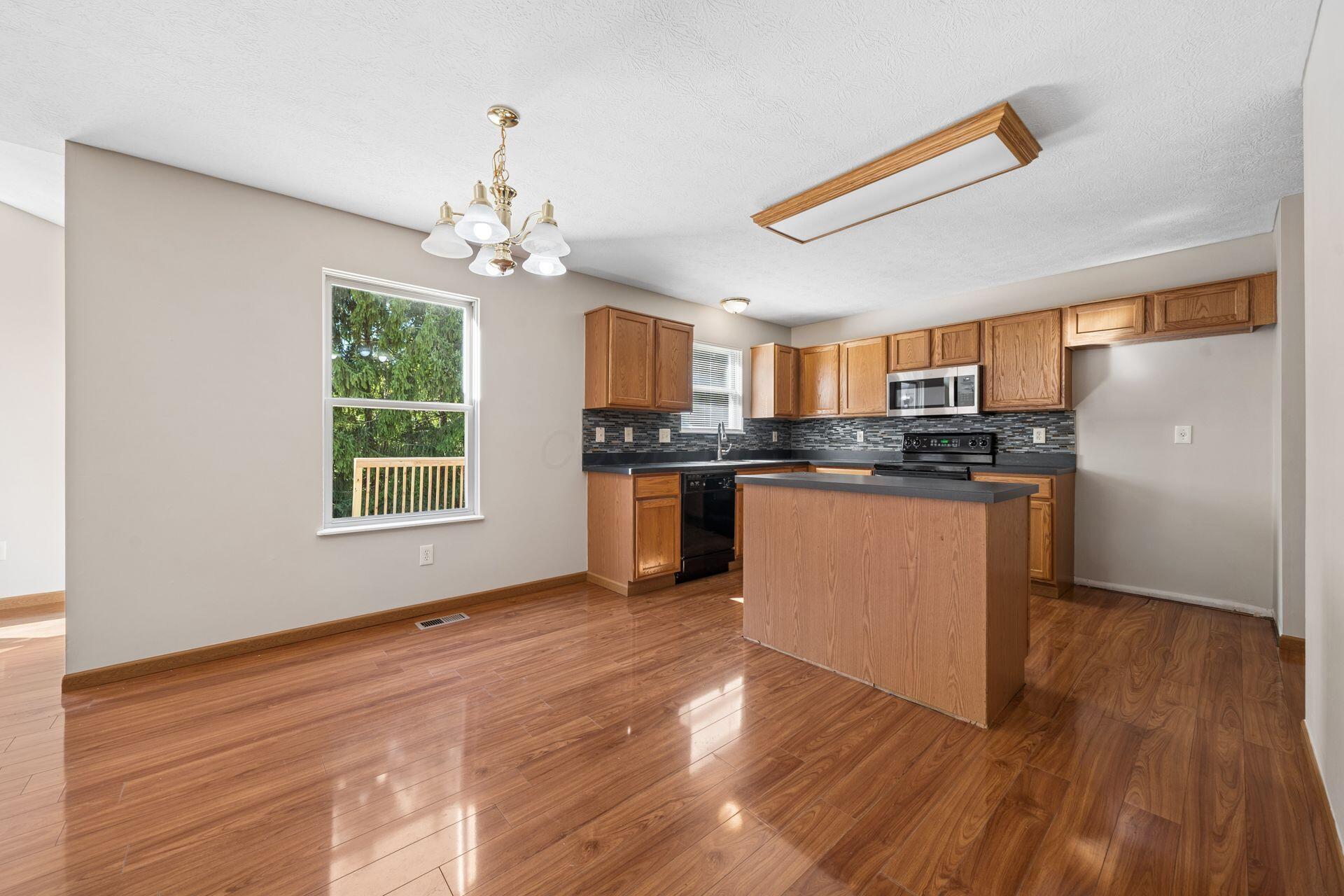 Kitchen with oak cabinets, dark counters, mosaic backsplash, and a central island beside a window.