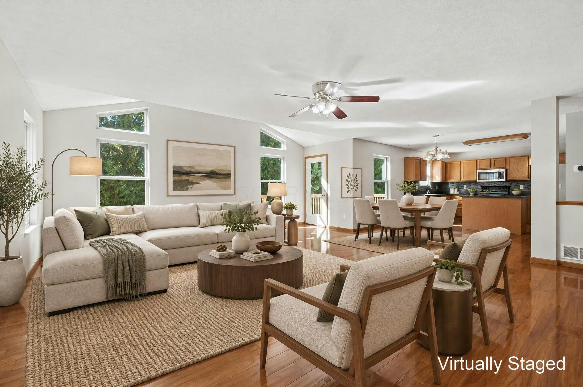 Virtually staged living room opening to a dining area and kitchen, with tall windows and wood floors.