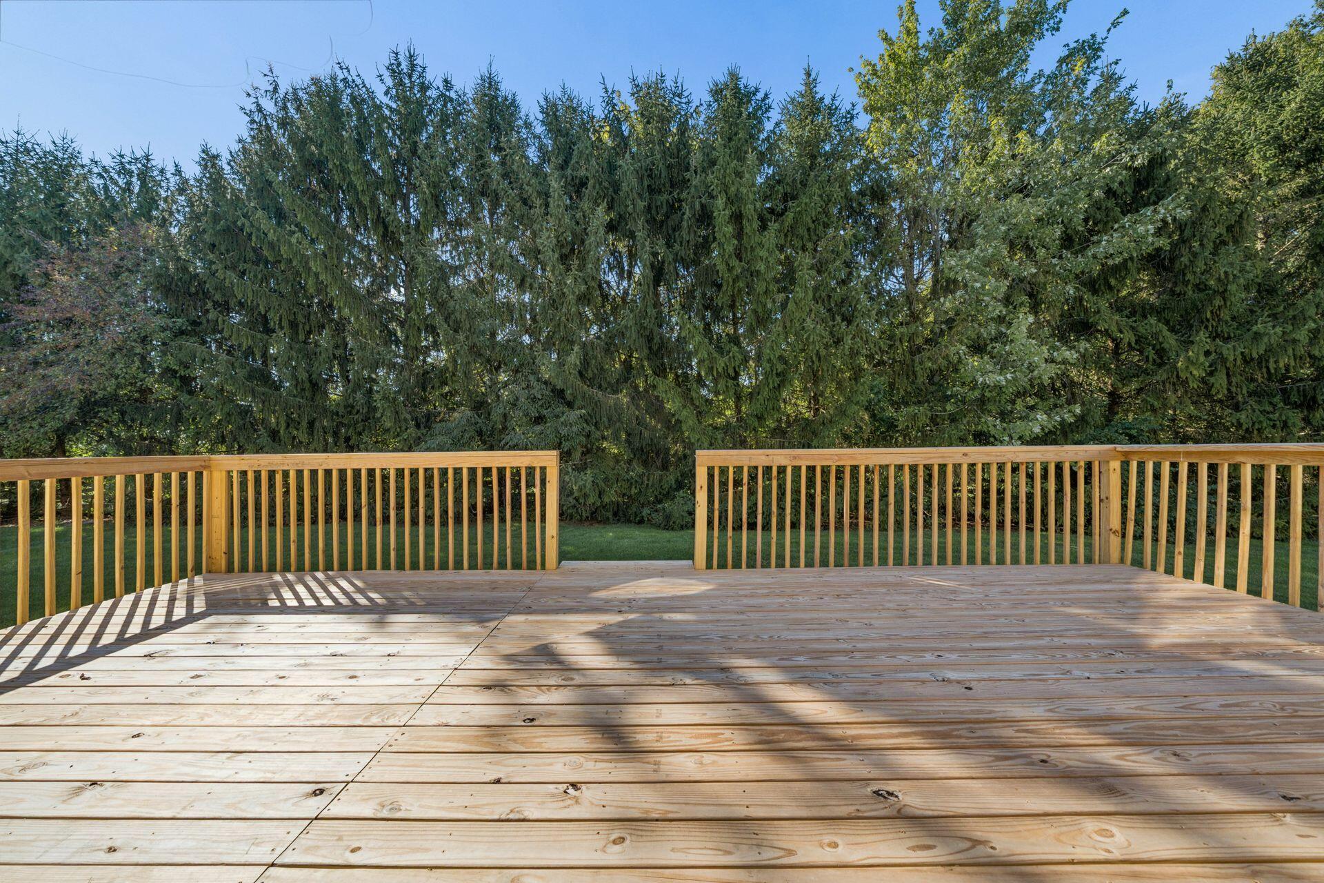 Spacious wooden deck overlooking a lawn and dense trees.