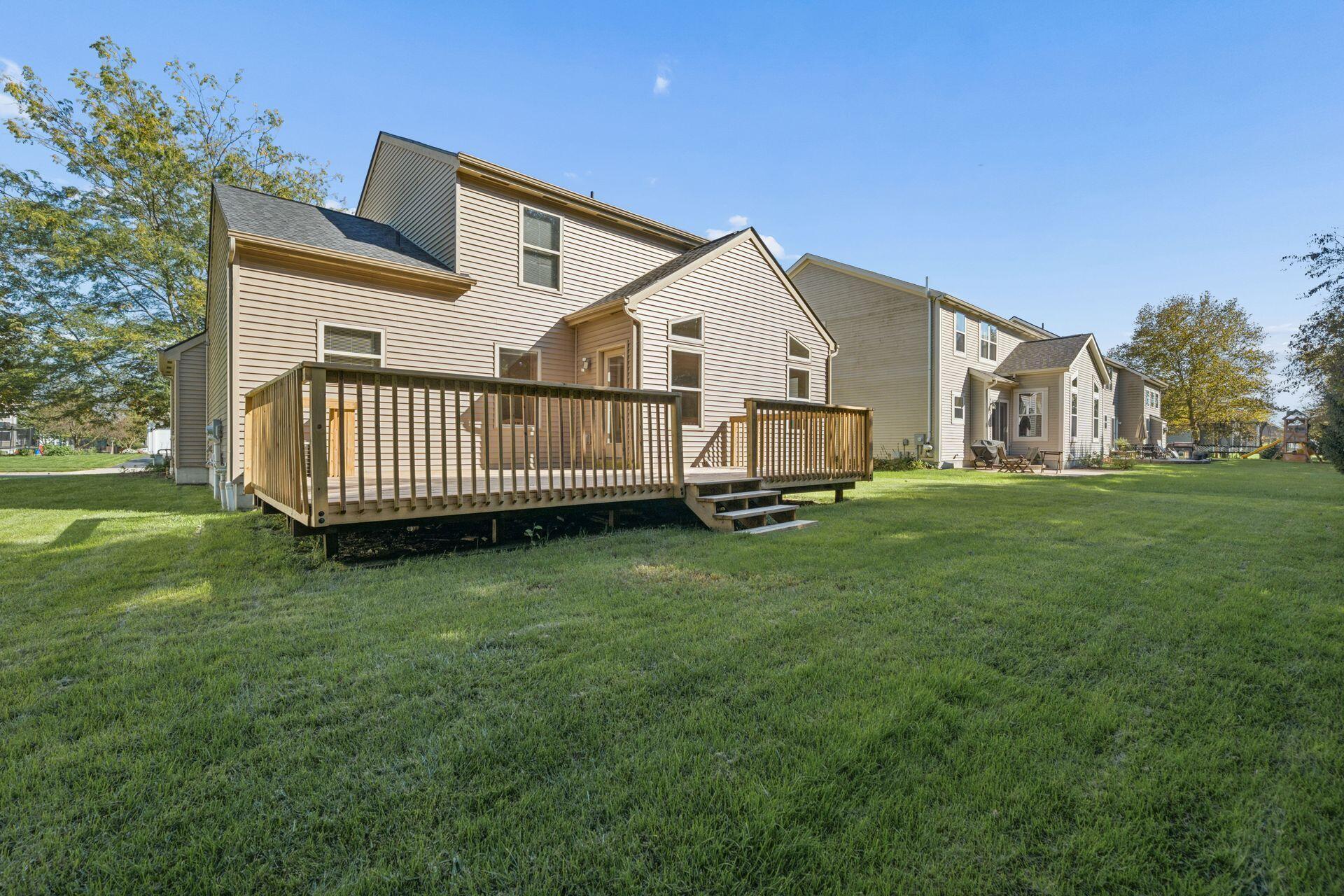 Rear of a beige two-story home with a raised wooden deck overlooking a broad lawn.