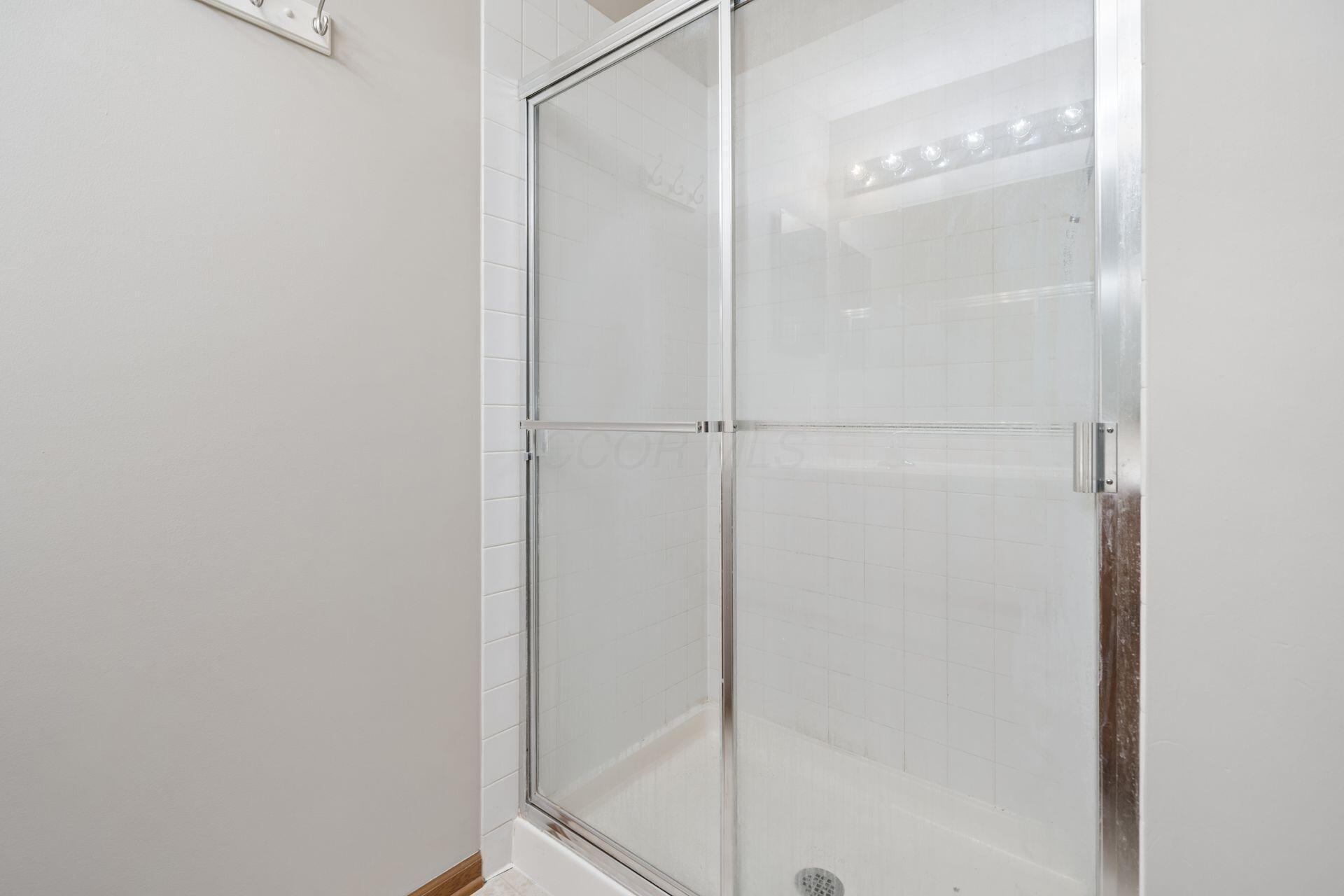 White-tiled bathroom shower with a clear glass enclosure and chrome framing.