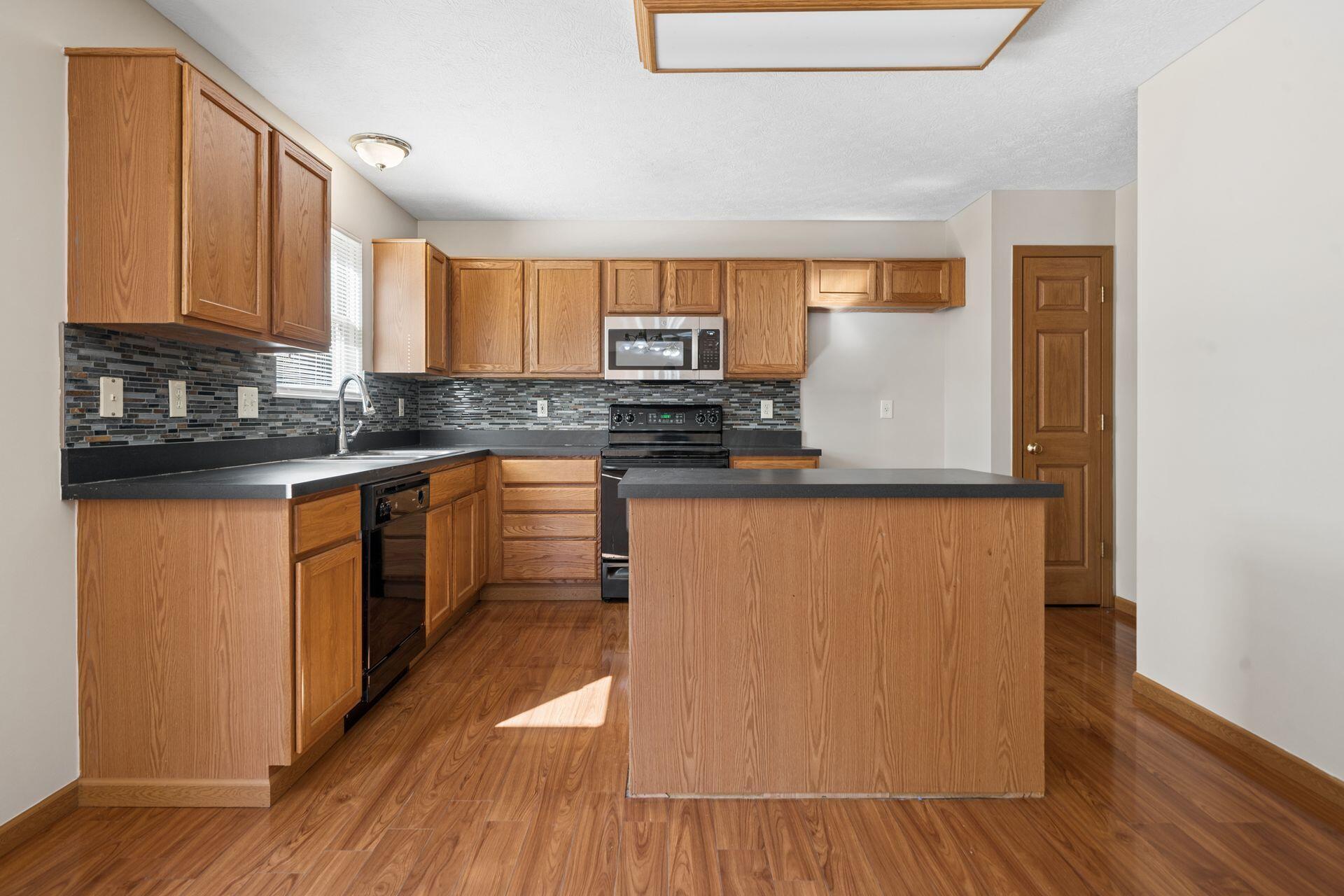 Kitchen with wood cabinets, a large island, dark mosaic backsplash, and wood-look flooring.