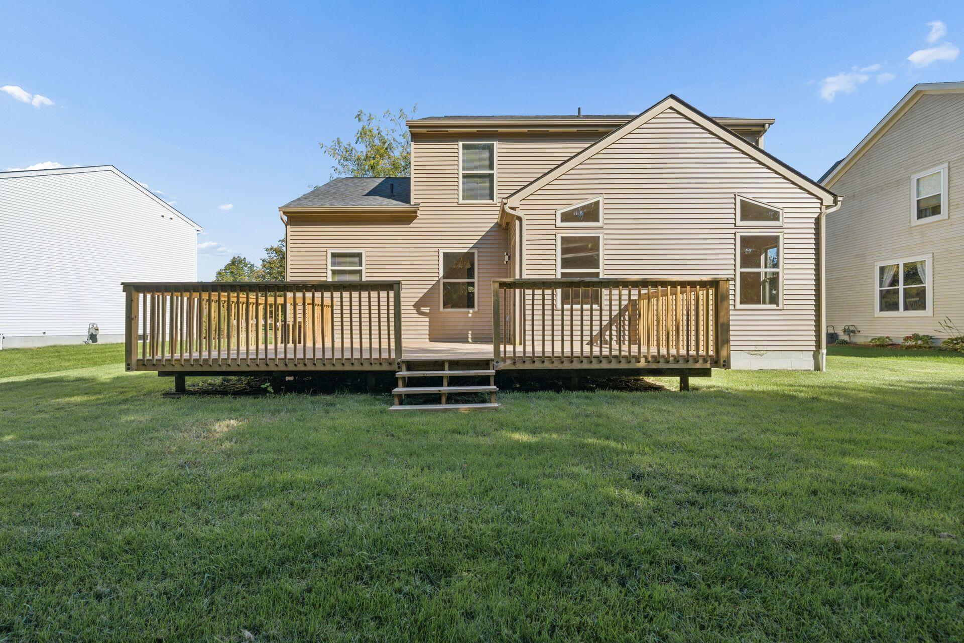 Rear of a two-story beige house with a broad raised wooden deck and central steps.