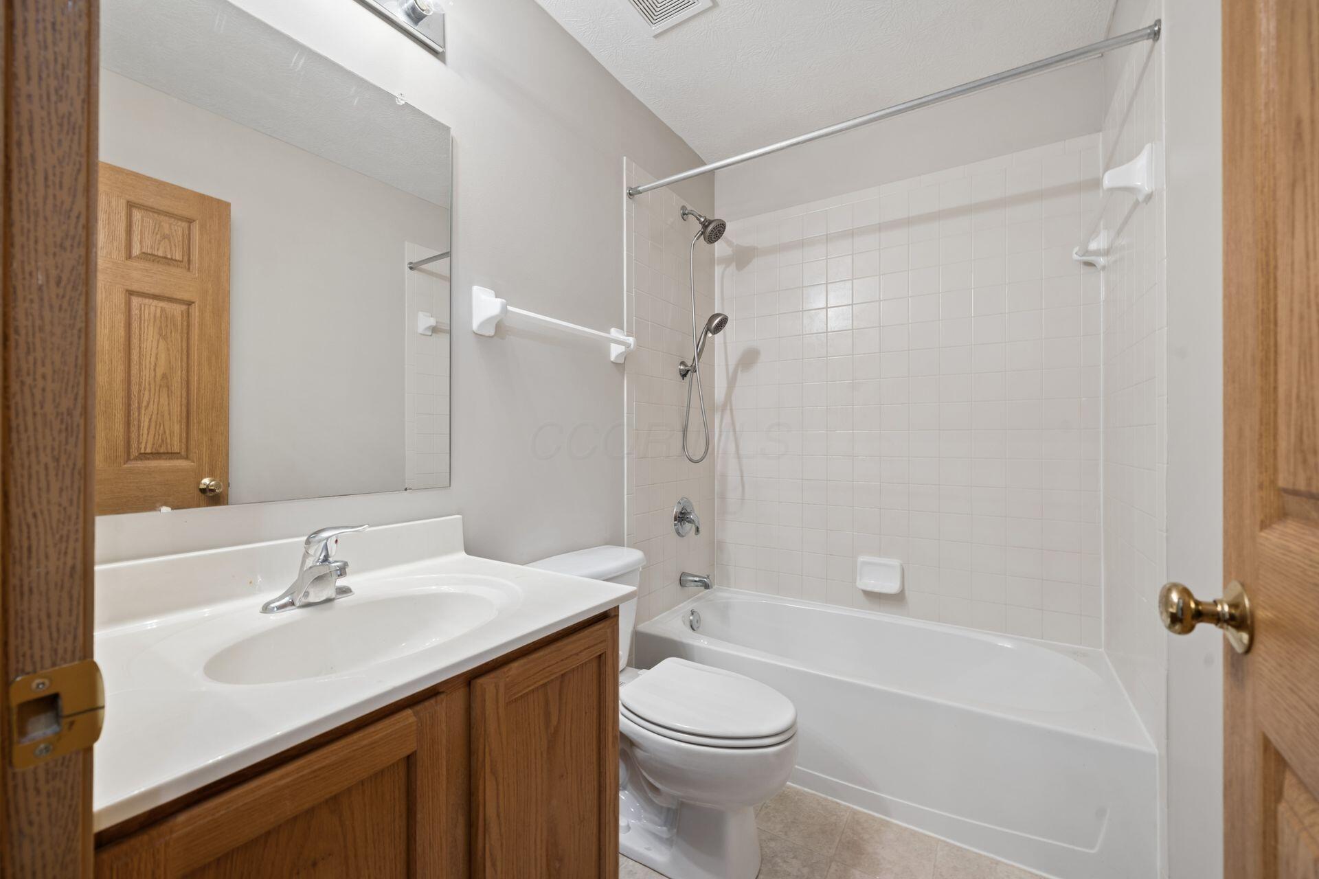 Bathroom with a white tub and tiled shower beside a wood vanity and toilet.