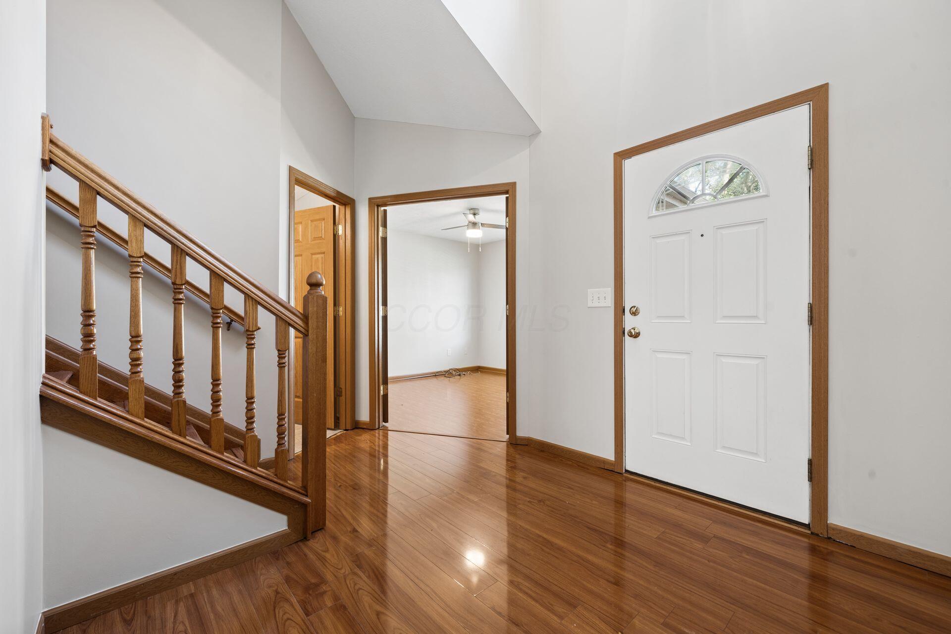 Entry foyer with a white front door, polished hardwood floors, and a wooden staircase.