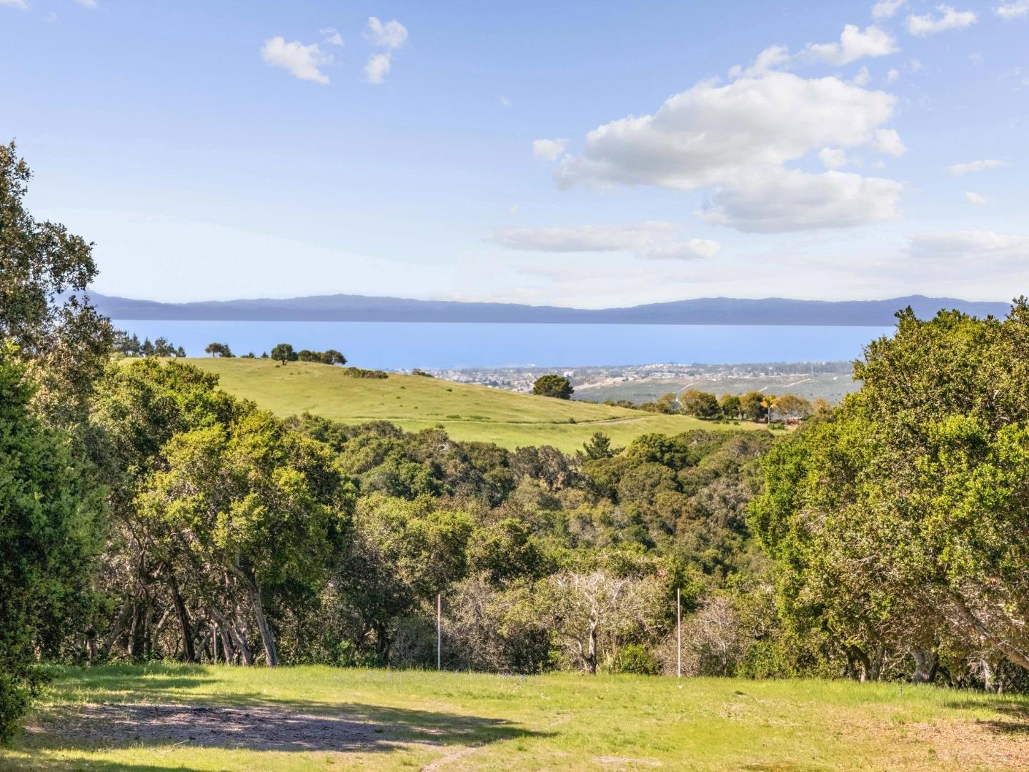 Open grassy land overlooks a coastal town, blue water, and distant mountain ridges.