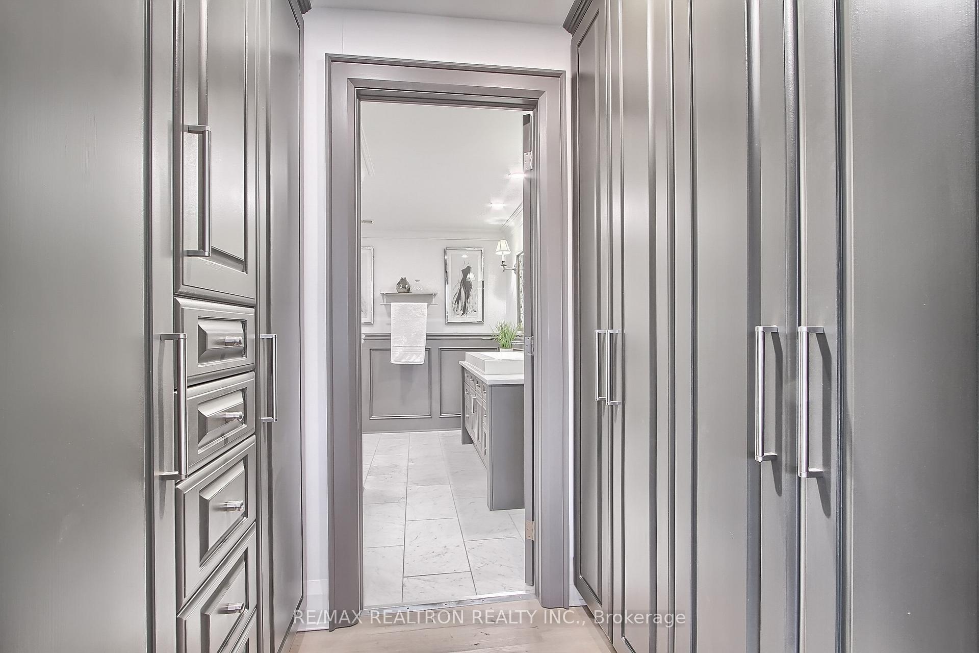 Bathroom beyond gray built-in cabinetry, with a white basin, paneled walls, and marble-look floor.