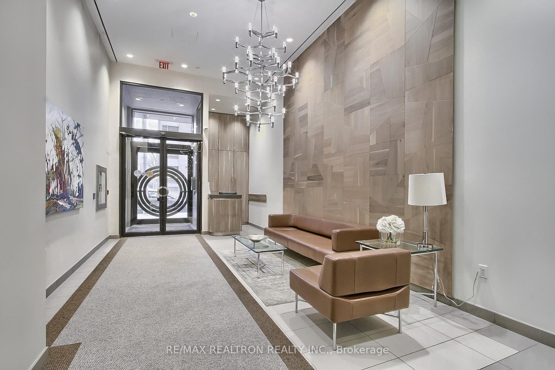 Condominium lobby with brown leather seating, a glass entrance, and a geometric wood-paneled wall.