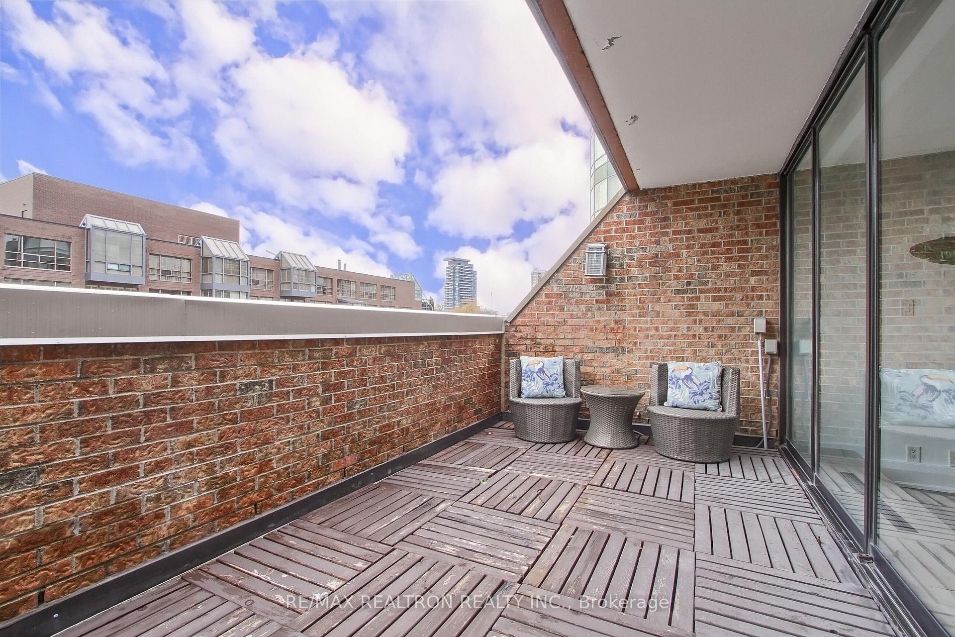 Condo terrace with wood decking, brick walls, and wicker seating overlooking nearby buildings.
