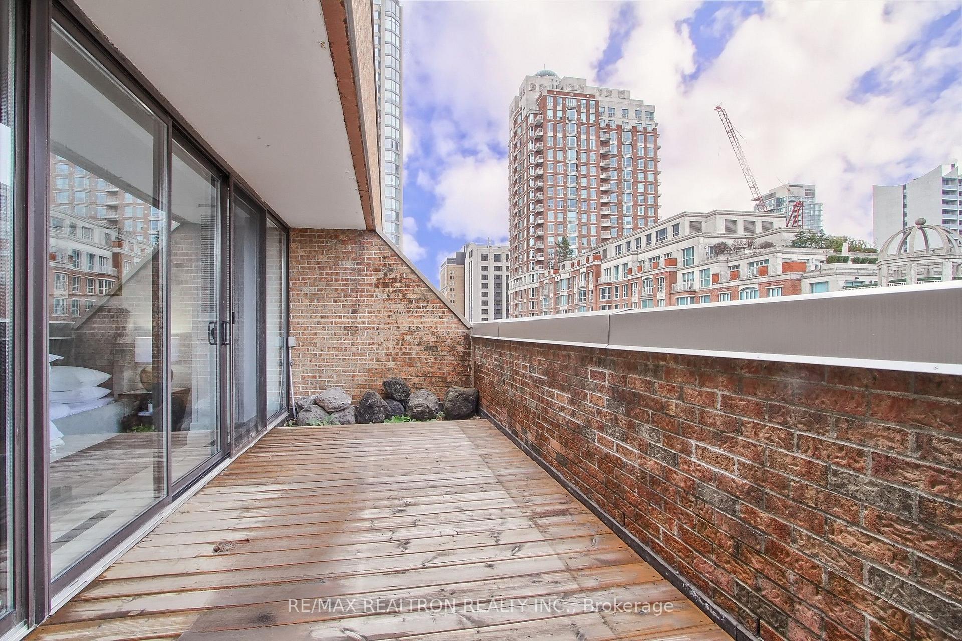 Condo terrace with wooden decking and brick walls overlooking high-rise buildings.