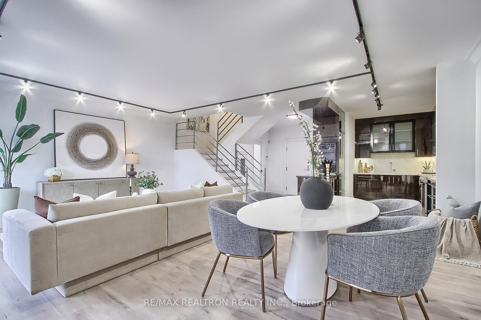Open-plan living and dining area with a beige sectional, round table, and modern staircase.