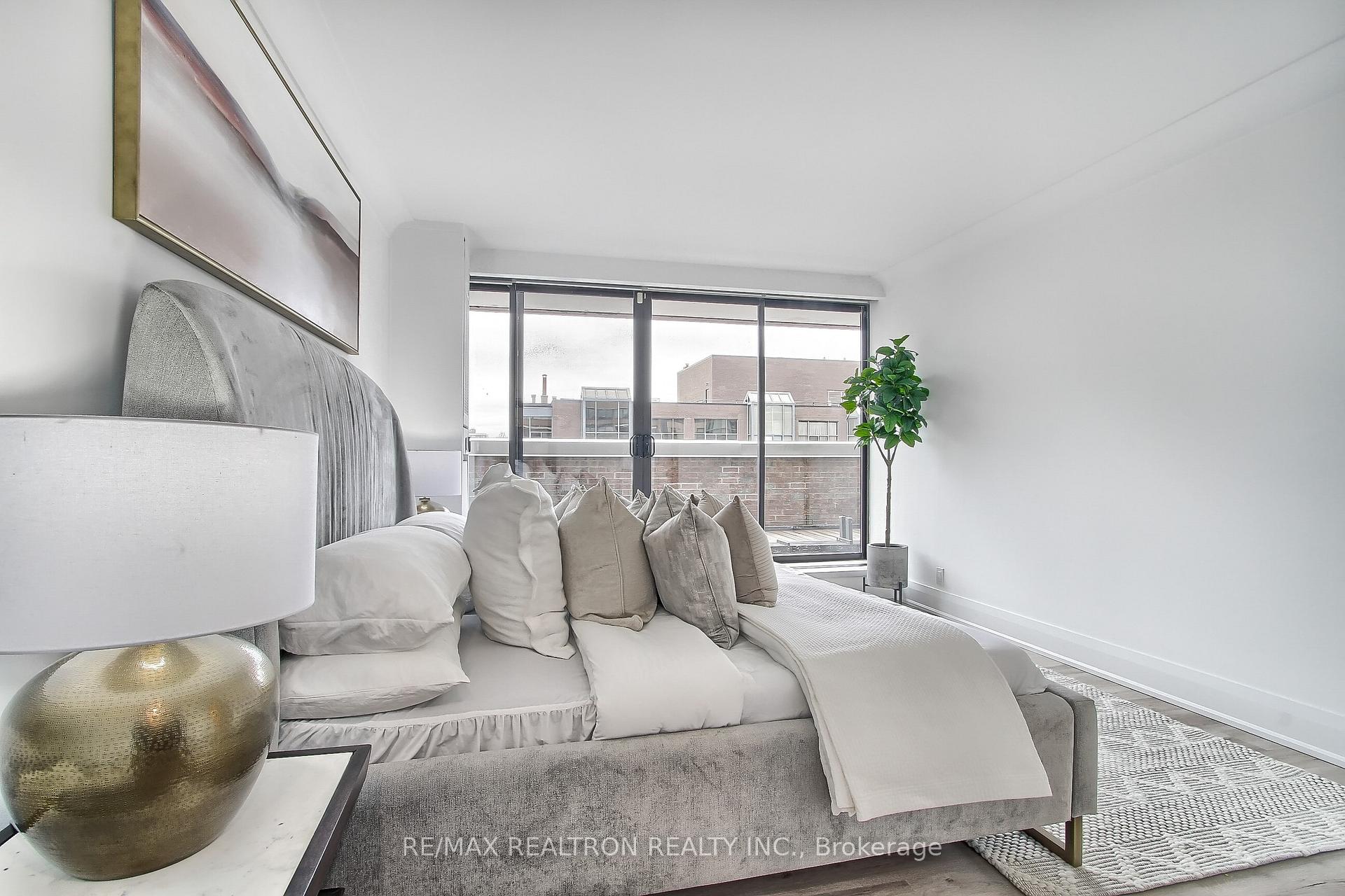 Bright staged bedroom with a gray upholstered bed, neutral pillows, and large sliding glass doors.