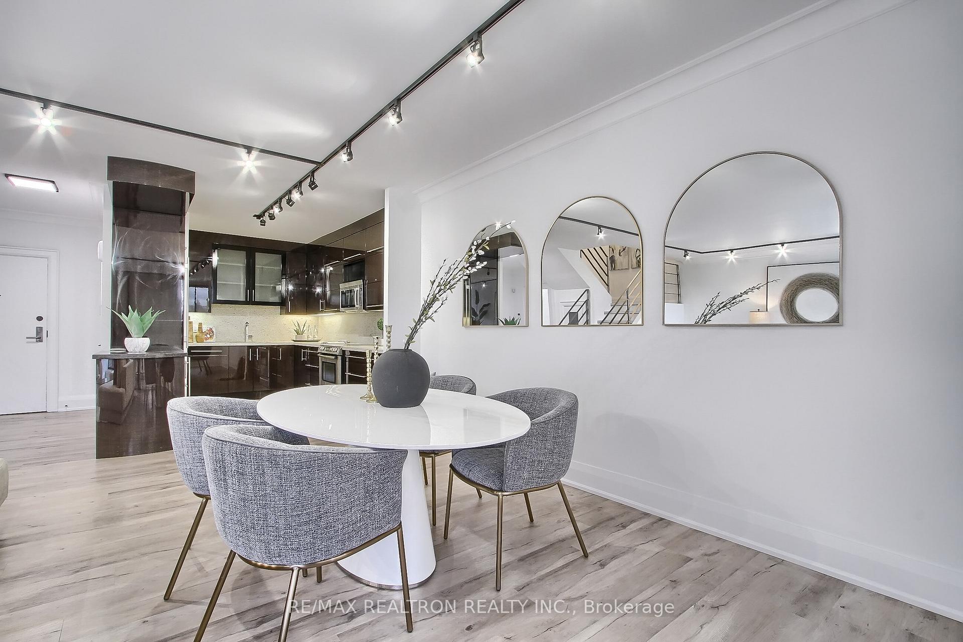 Staged condo dining area with a round white table, gray chairs, and an open modern kitchen.