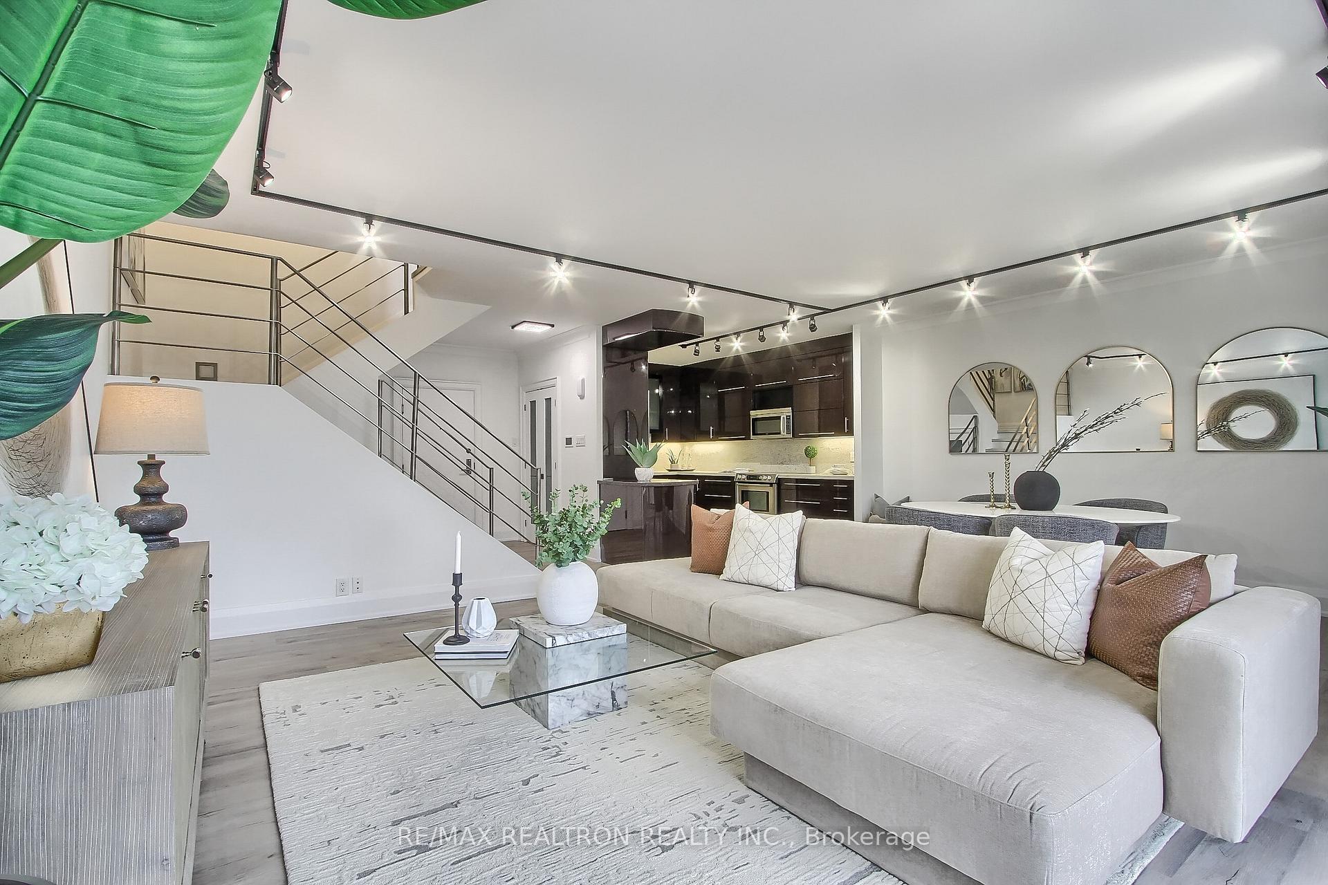 Staged living room with a large beige sectional, open kitchen, dining area, and staircase.