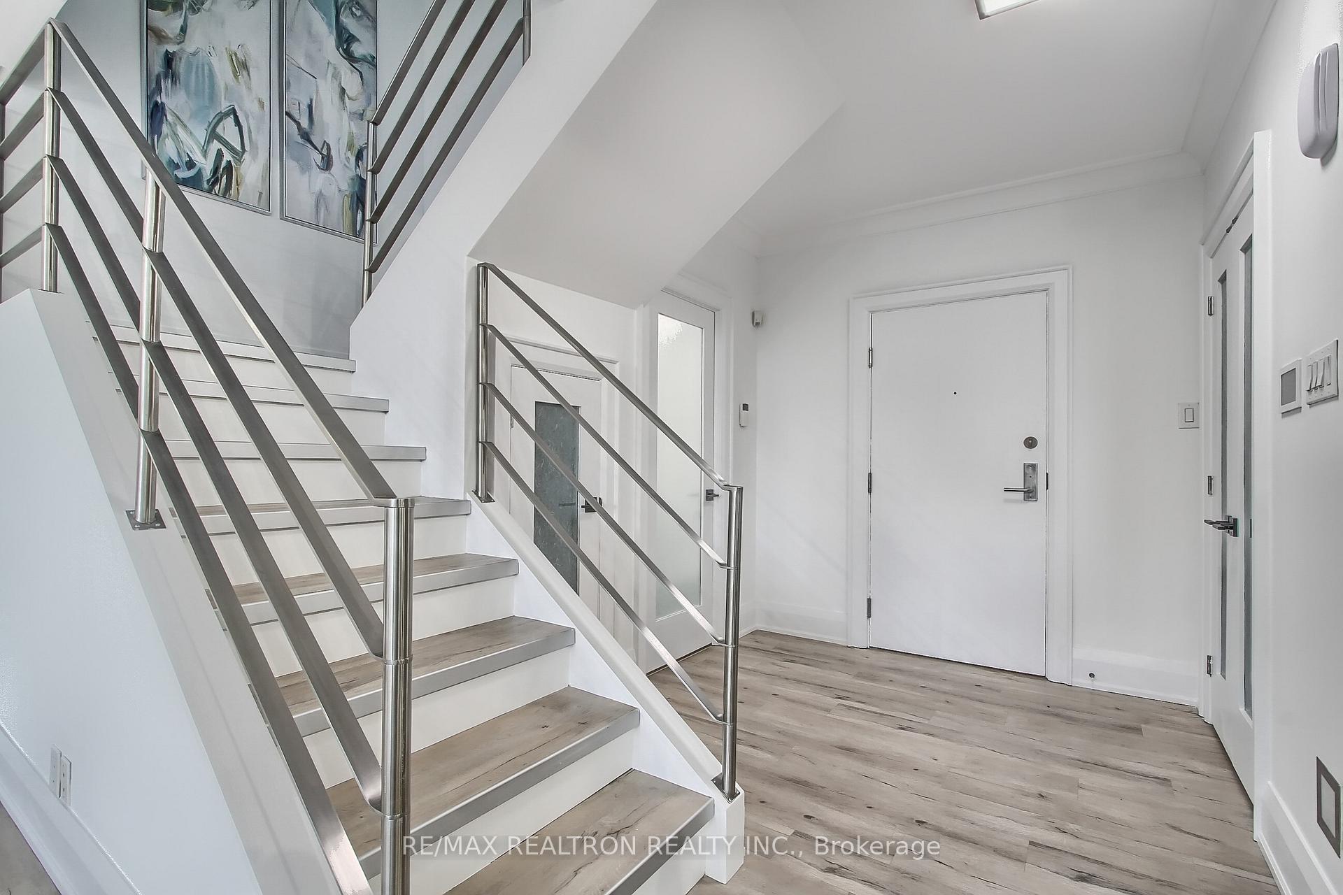 Condo entry foyer with a stainless-steel-railed staircase, light wood flooring, and abstract artwork.
