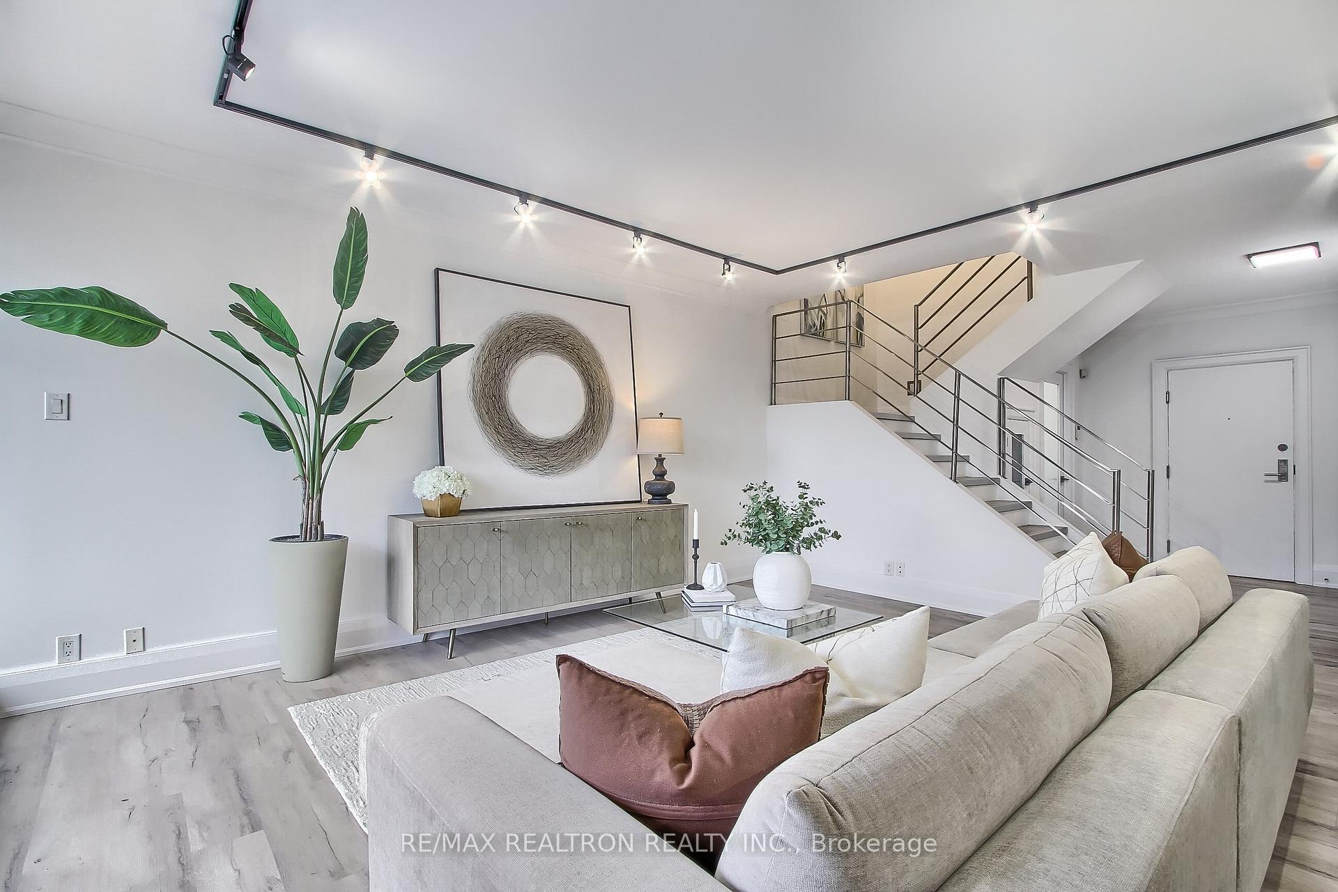 Staged living room with a cream sectional sofa and a staircase with metal railings.