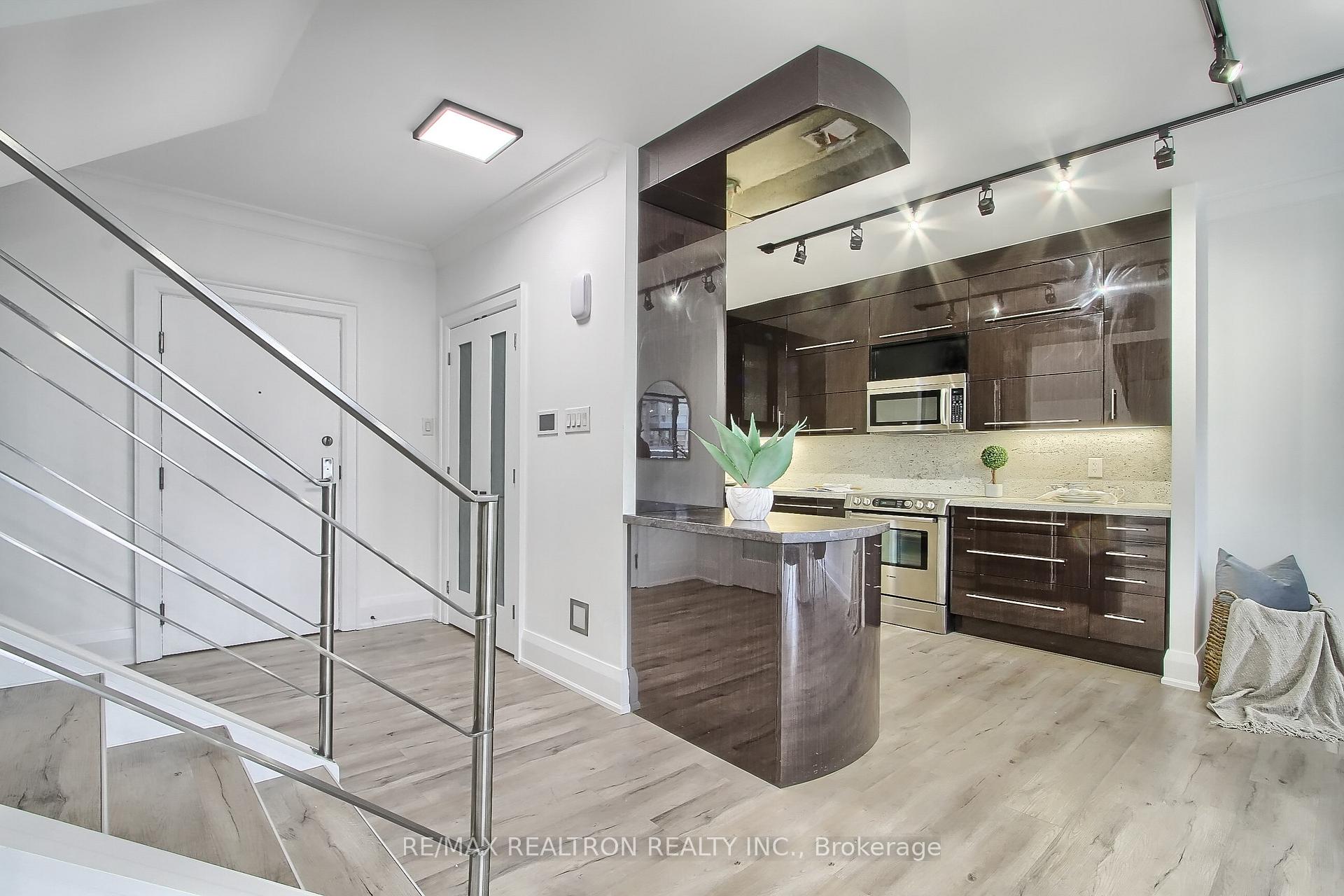 Condo kitchen with dark wood cabinets, stainless steel appliances, and a curved peninsula beside the entryway.
