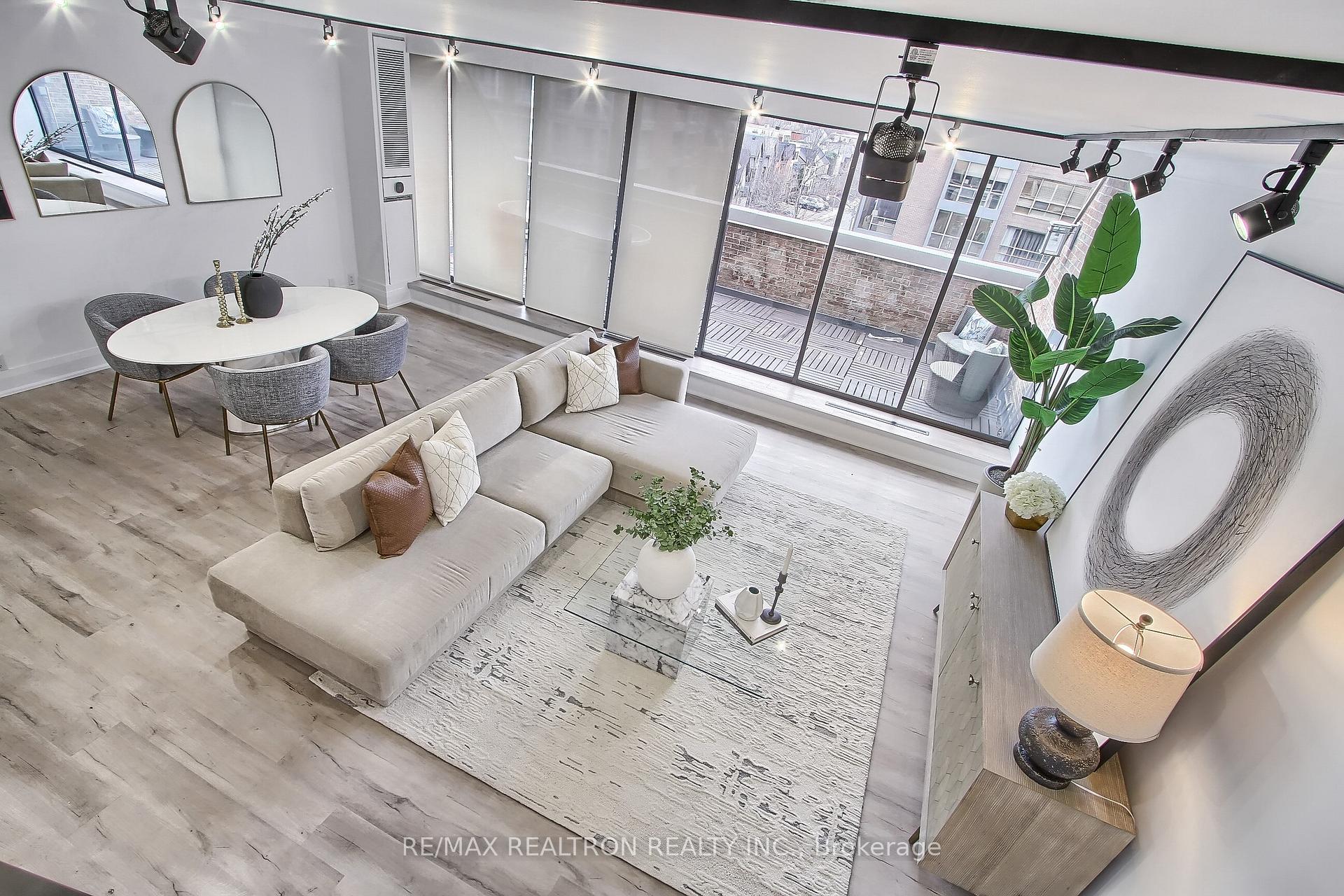 Staged condo living and dining area with a cream sectional and balcony-facing sliding glass doors.