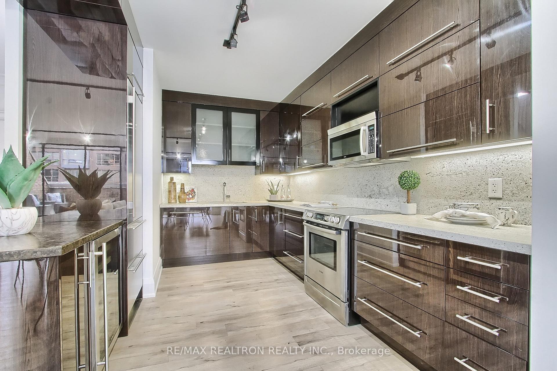 Modern condo kitchen with dark glossy cabinetry, pale stone counters, and stainless steel appliances.