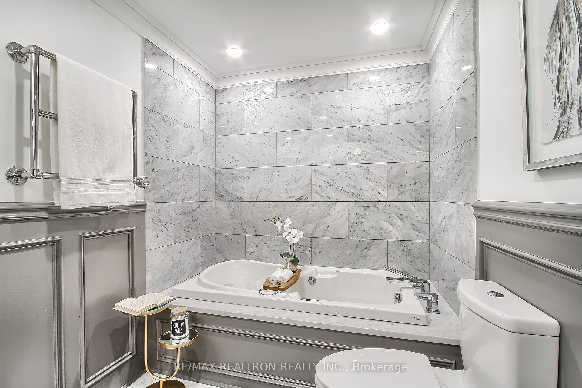 Bathroom with a white soaking tub, marble tile surround, gray paneled wainscoting, and chrome towel bars.