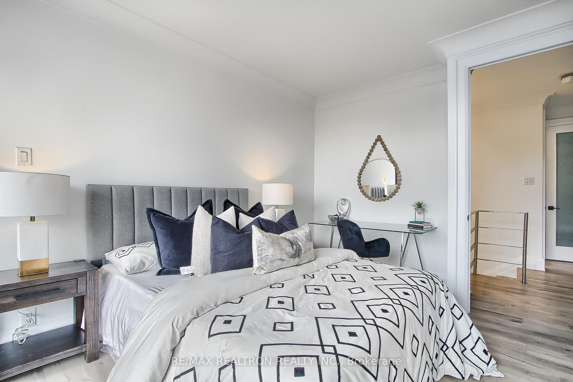 Furnished bedroom with geometric bedding, a gray upholstered headboard, and a glass desk.