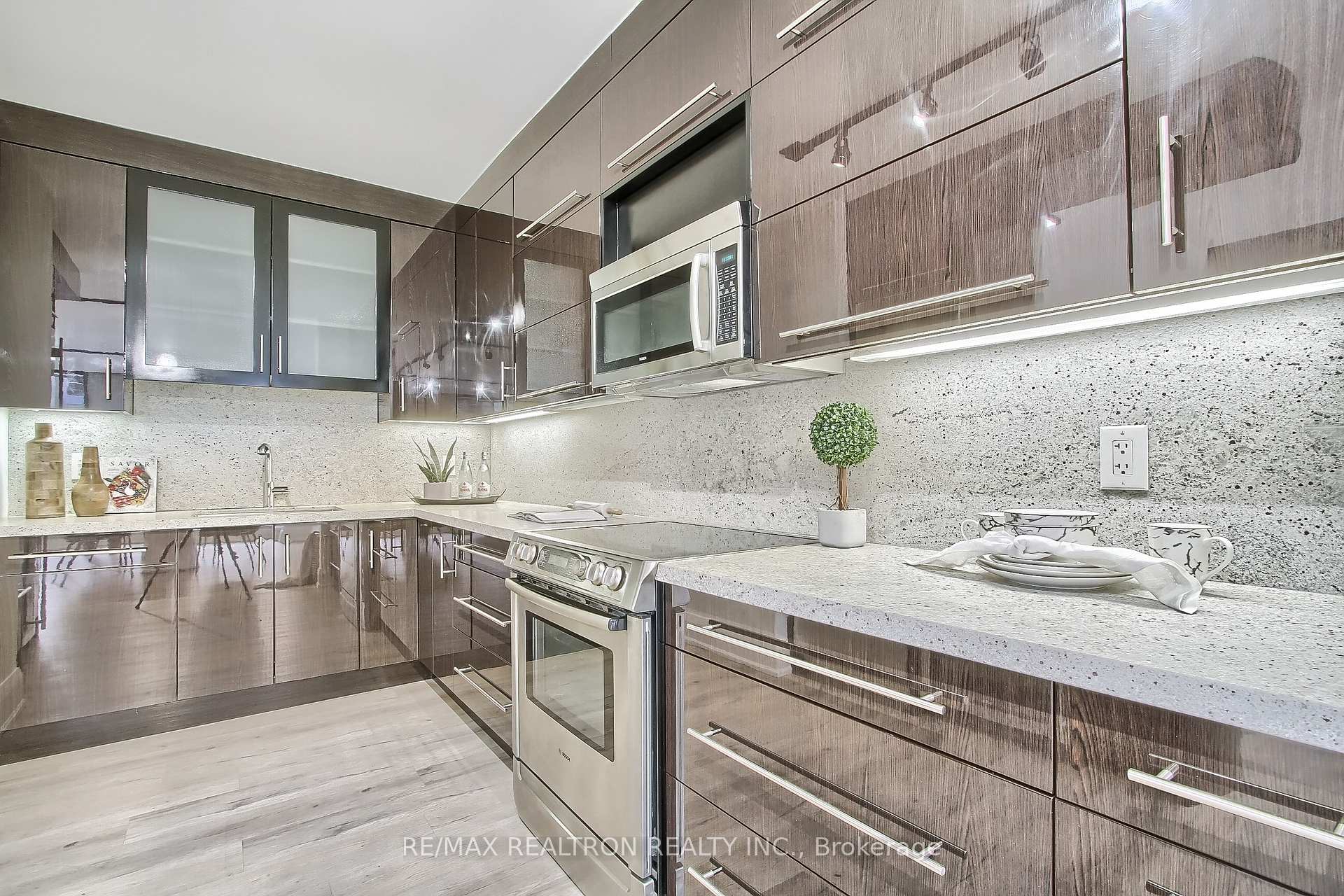 Modern kitchen with glossy dark cabinets, stone counters, and stainless steel appliances.