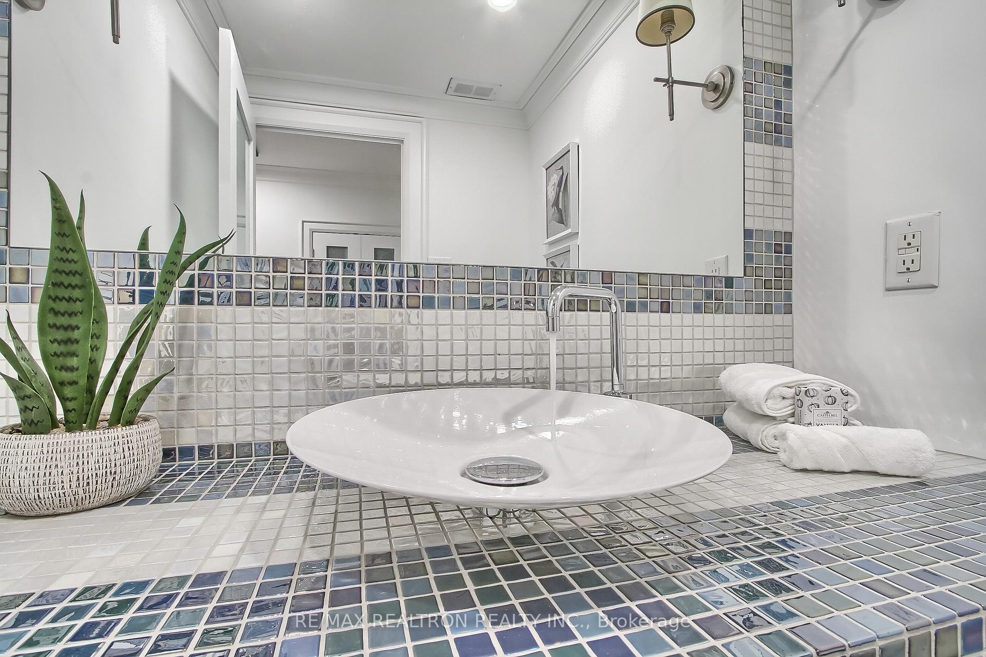 Bathroom vanity with a white vessel sink, chrome faucet, and blue-gray mosaic tile.