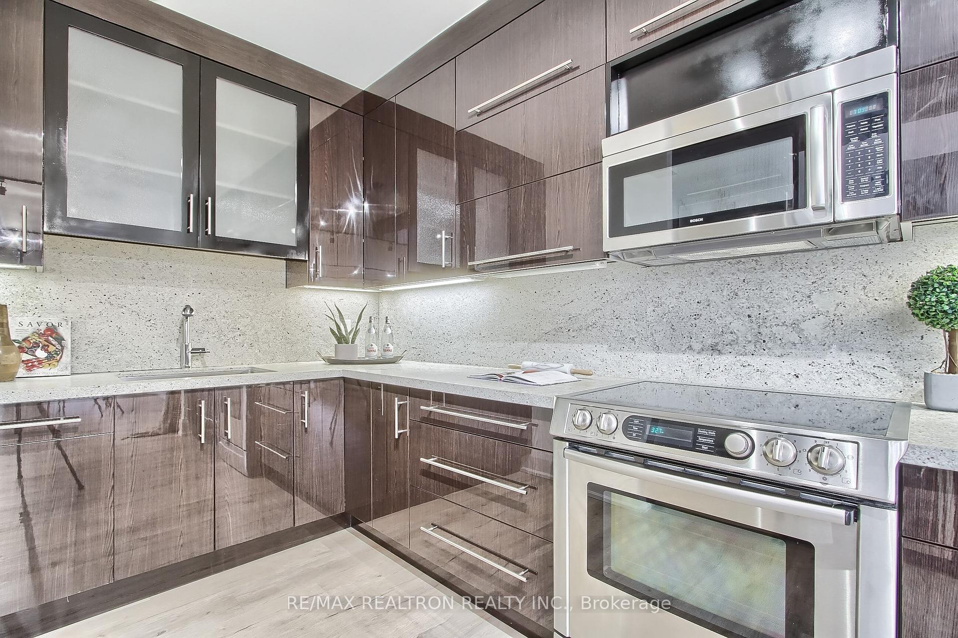 Modern kitchen with glossy dark wood cabinets, pale stone counters, and stainless-steel appliances.