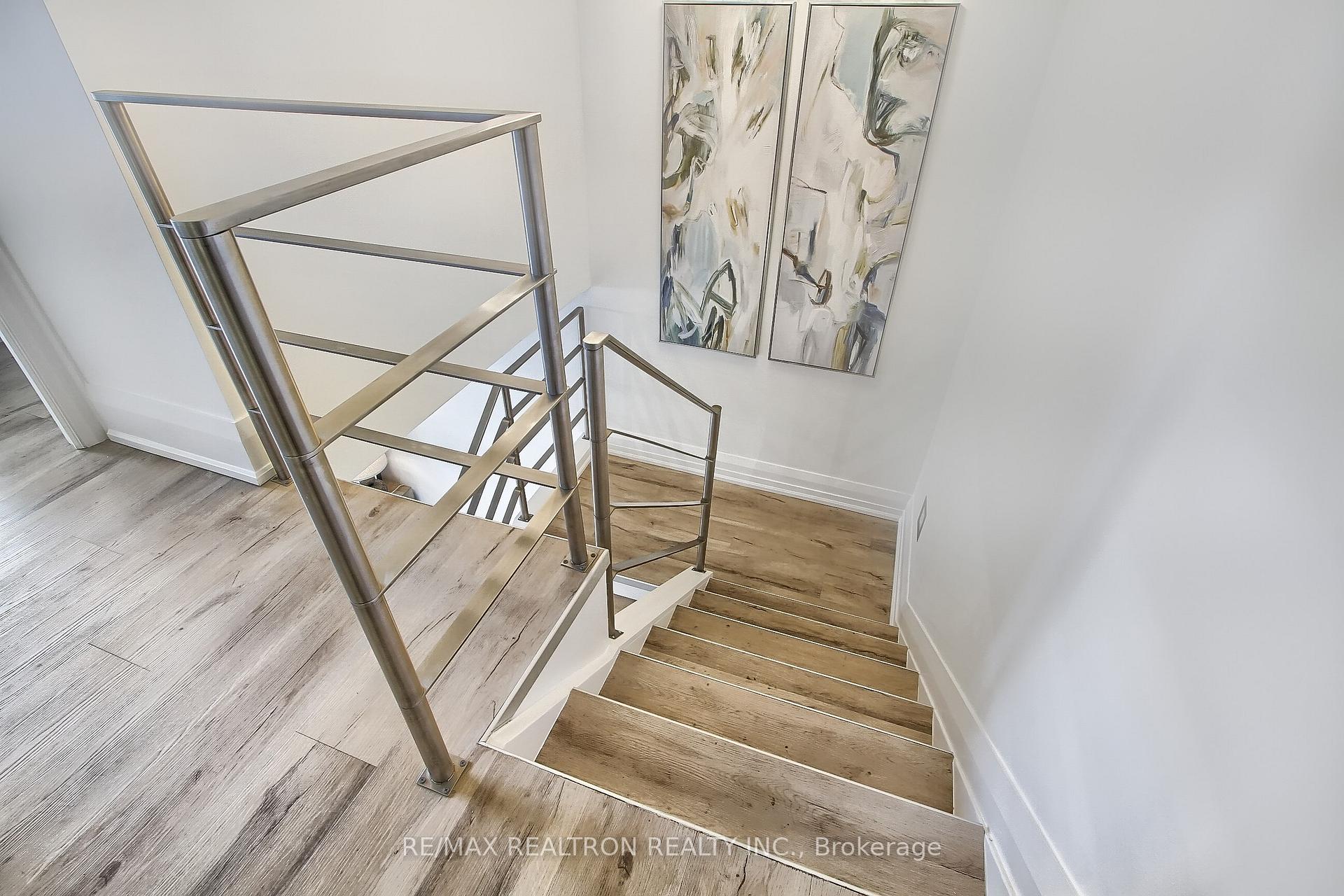 Wood-finished staircase with stainless-steel railings and abstract paintings on the wall.