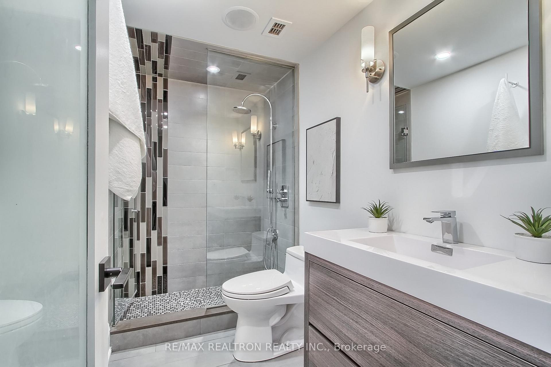 Modern bathroom with glass walk-in shower, gray tile, and a long double-sink vanity.
