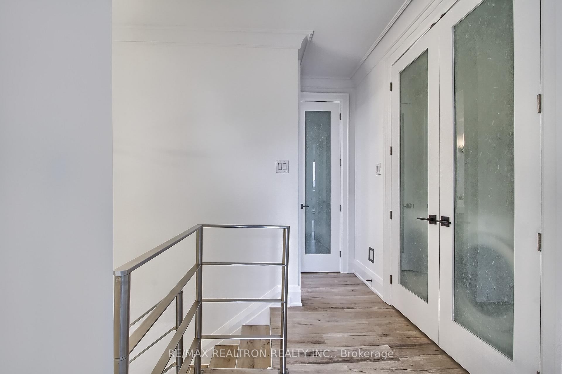 Bright hallway with frosted-glass doors, wood-look flooring, and a metal stair railing.