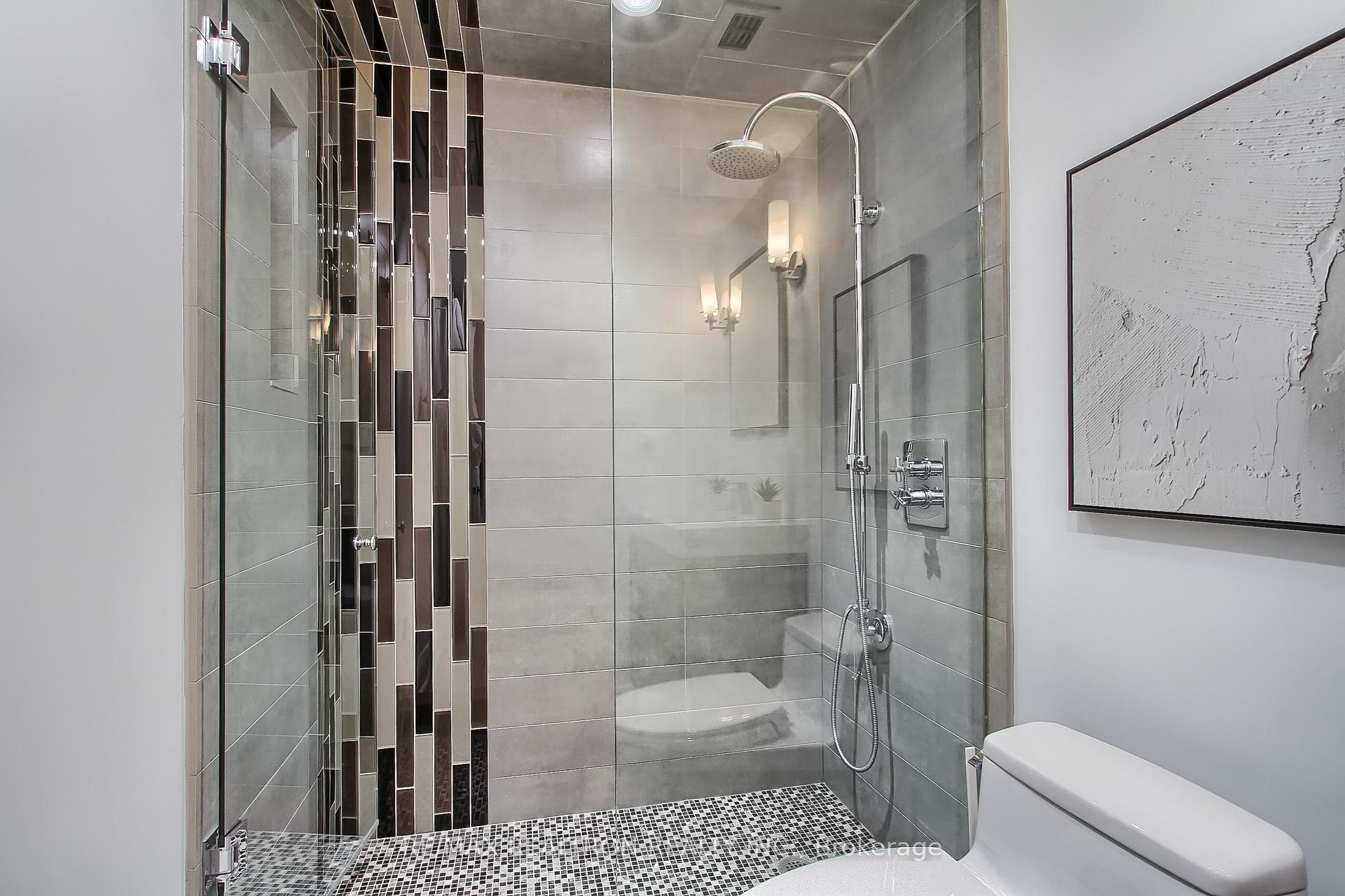 Modern bathroom with a glass walk-in shower, gray tile, and dark mosaic accents.