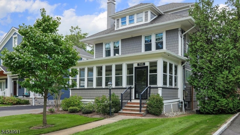 Gray-shingled two-story house with an enclosed front porch and landscaped front lawn.