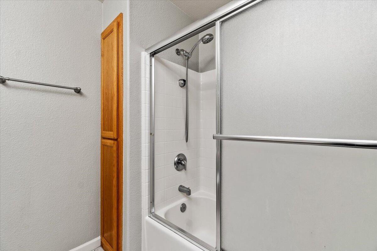 Bathroom with a white bathtub, sliding glass shower doors, and a narrow wooden cabinet.