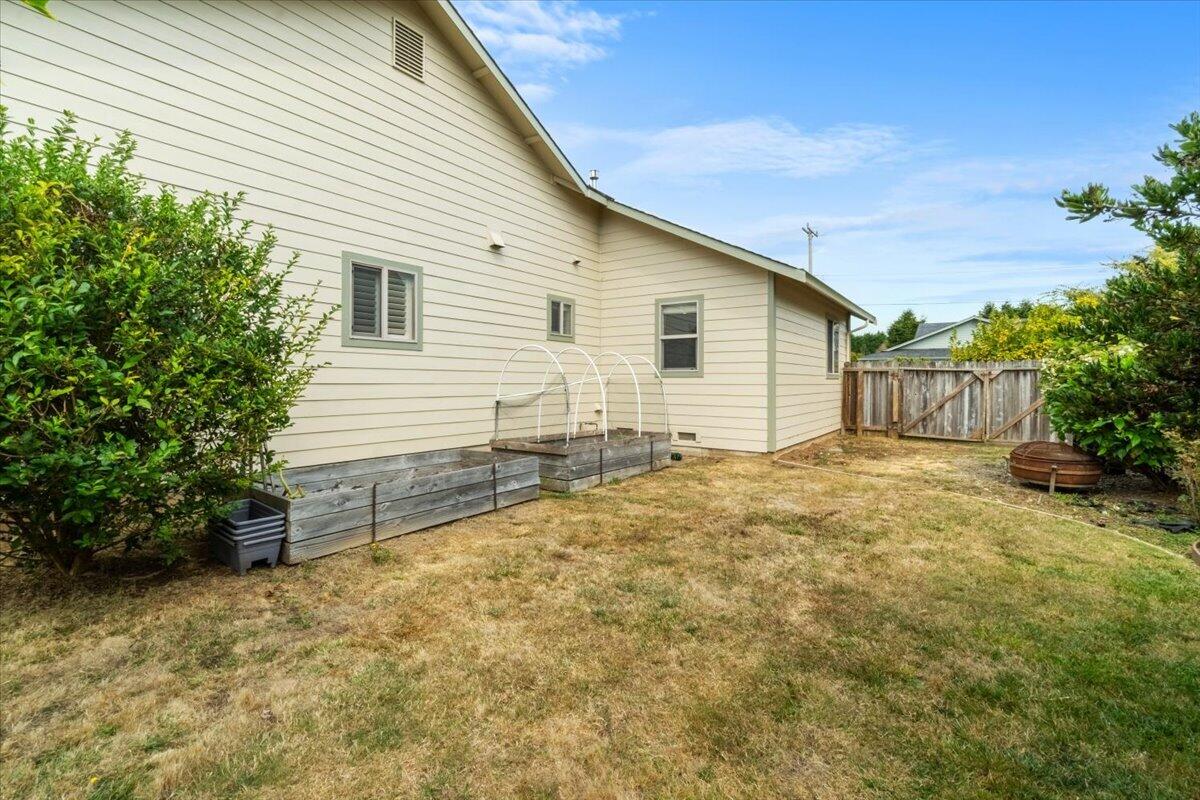 Side of a light-colored house beside raised garden beds and a dry lawn.