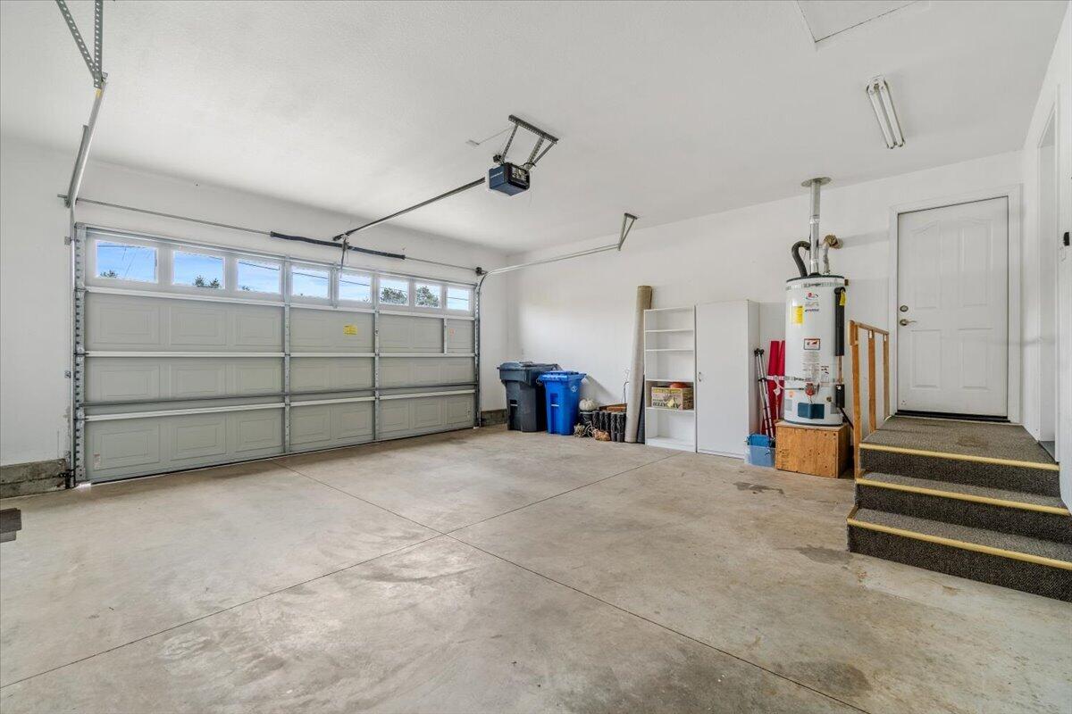 Spacious garage with a wide windowed garage door, concrete floor, and carpeted steps to the entry door.