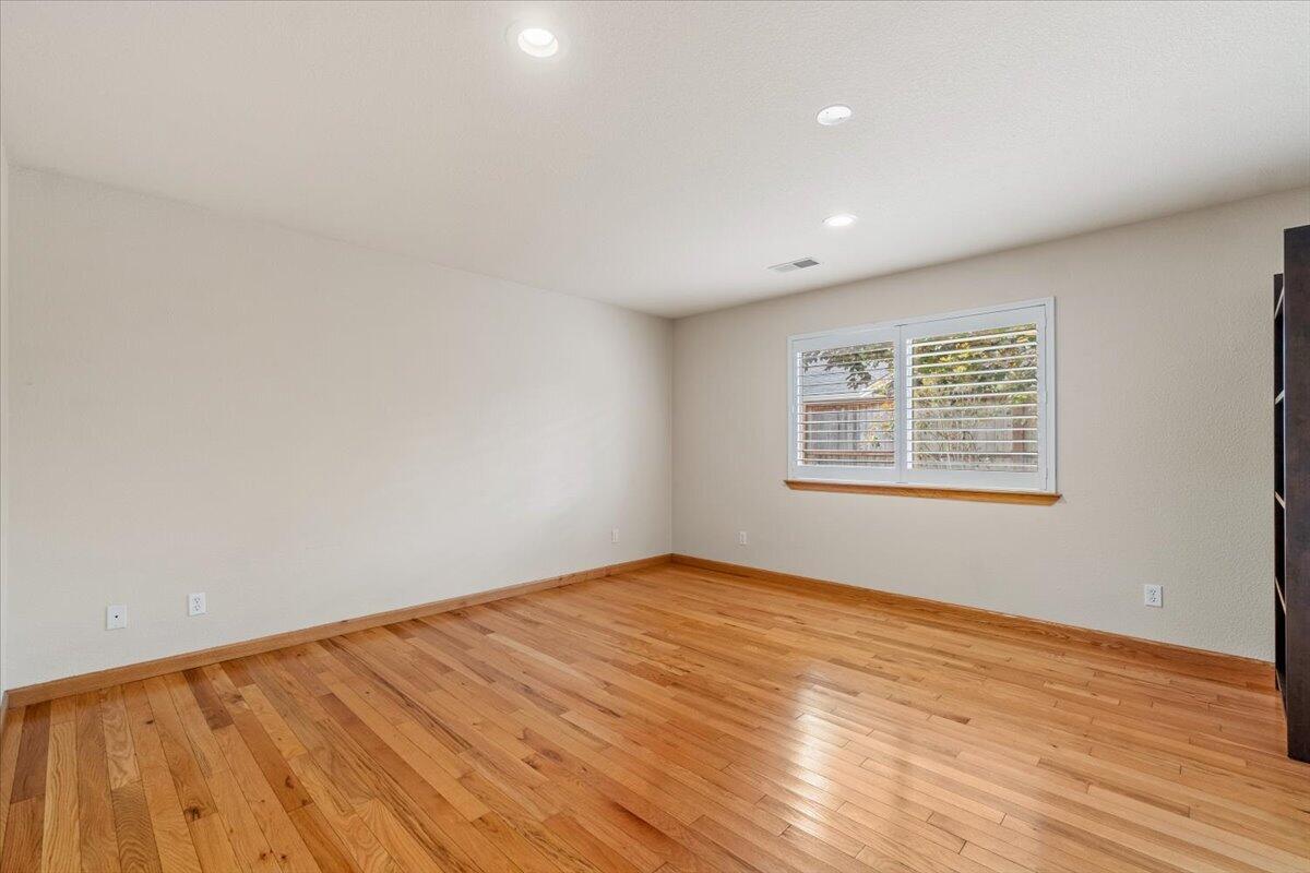Empty bedroom with hardwood floors and a wide window fitted with white plantation shutters.