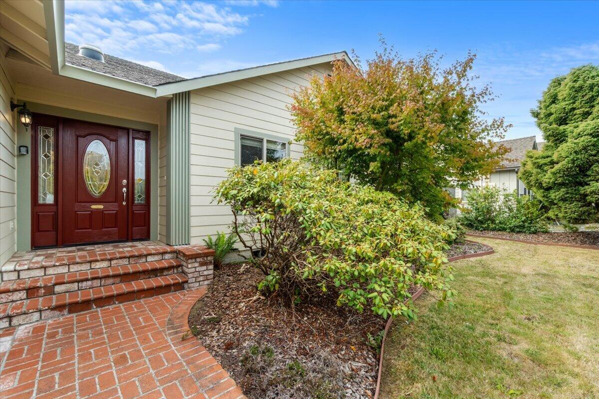 Home entrance with a red glass-paneled door, brick steps, and landscaped shrubs.