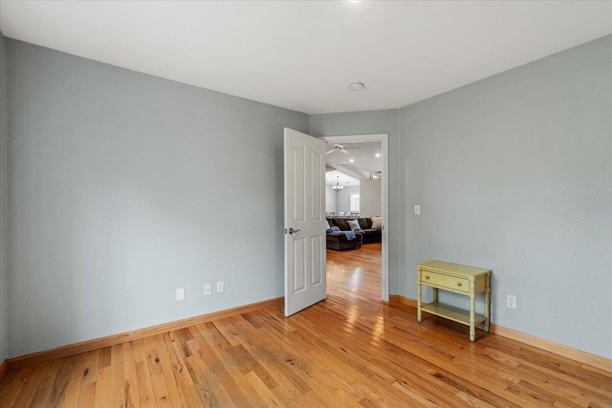 Mostly empty room with hardwood floors, pale blue-gray walls, and an open doorway to the living room.