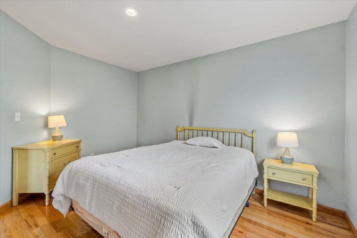 Bedroom with a white-quilted bed, light wood furniture, and warm hardwood floors.