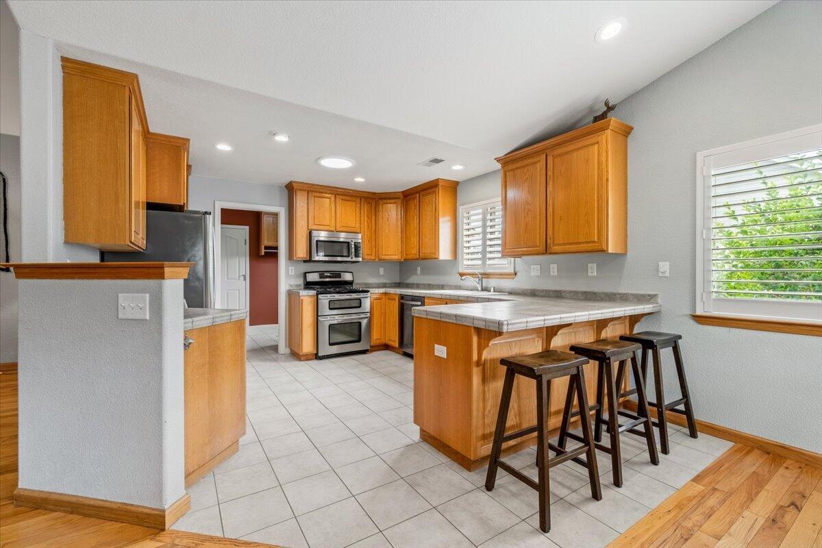 Kitchen with wood cabinets, stainless appliances, and a tiled island with bar stools.