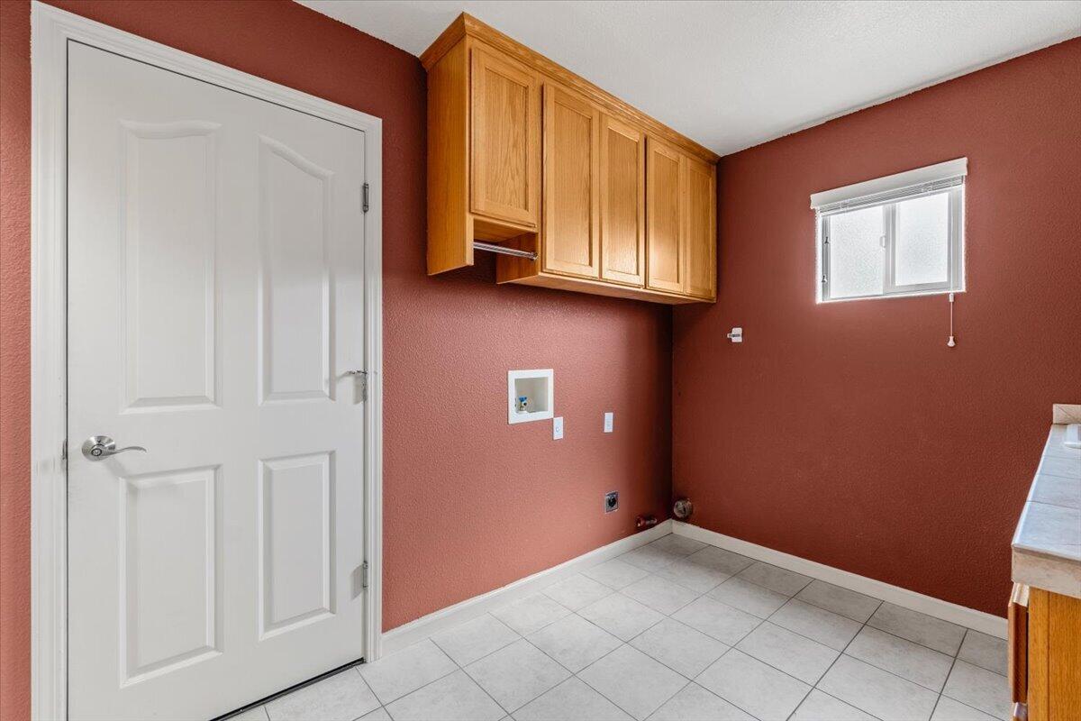 Laundry room with terracotta walls, white tile floor, overhead wooden cabinets, and washer hookups.
