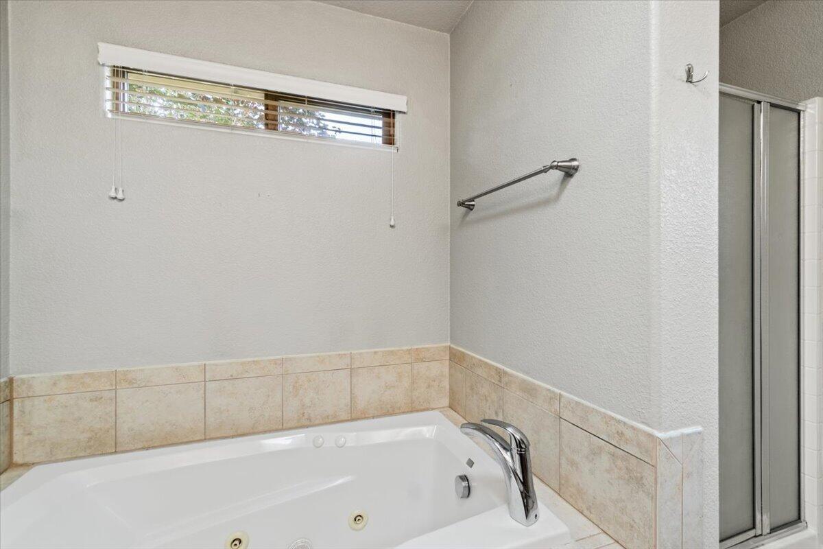 Bathroom with a jetted tub, beige tile surround, and glass shower enclosure.