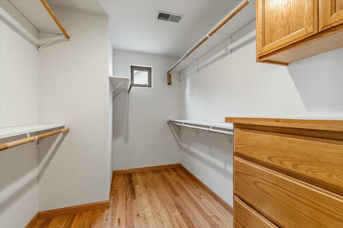 Walk-in closet with hardwood floors, open shelving, and built-in wooden drawers and cabinets.