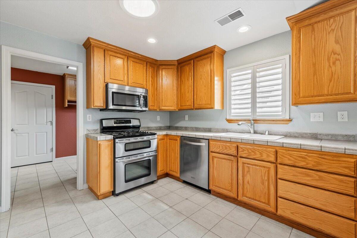 Kitchen with honey-colored wood cabinets, stainless steel appliances, and a sink beneath shuttered windows.