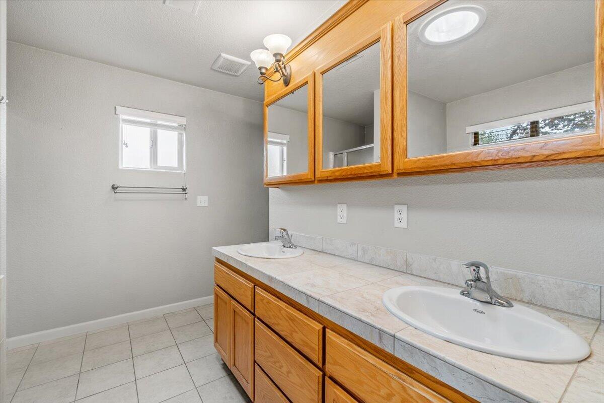 Bathroom with a long double-sink vanity, oak cabinets, framed mirrors, and tiled floors.