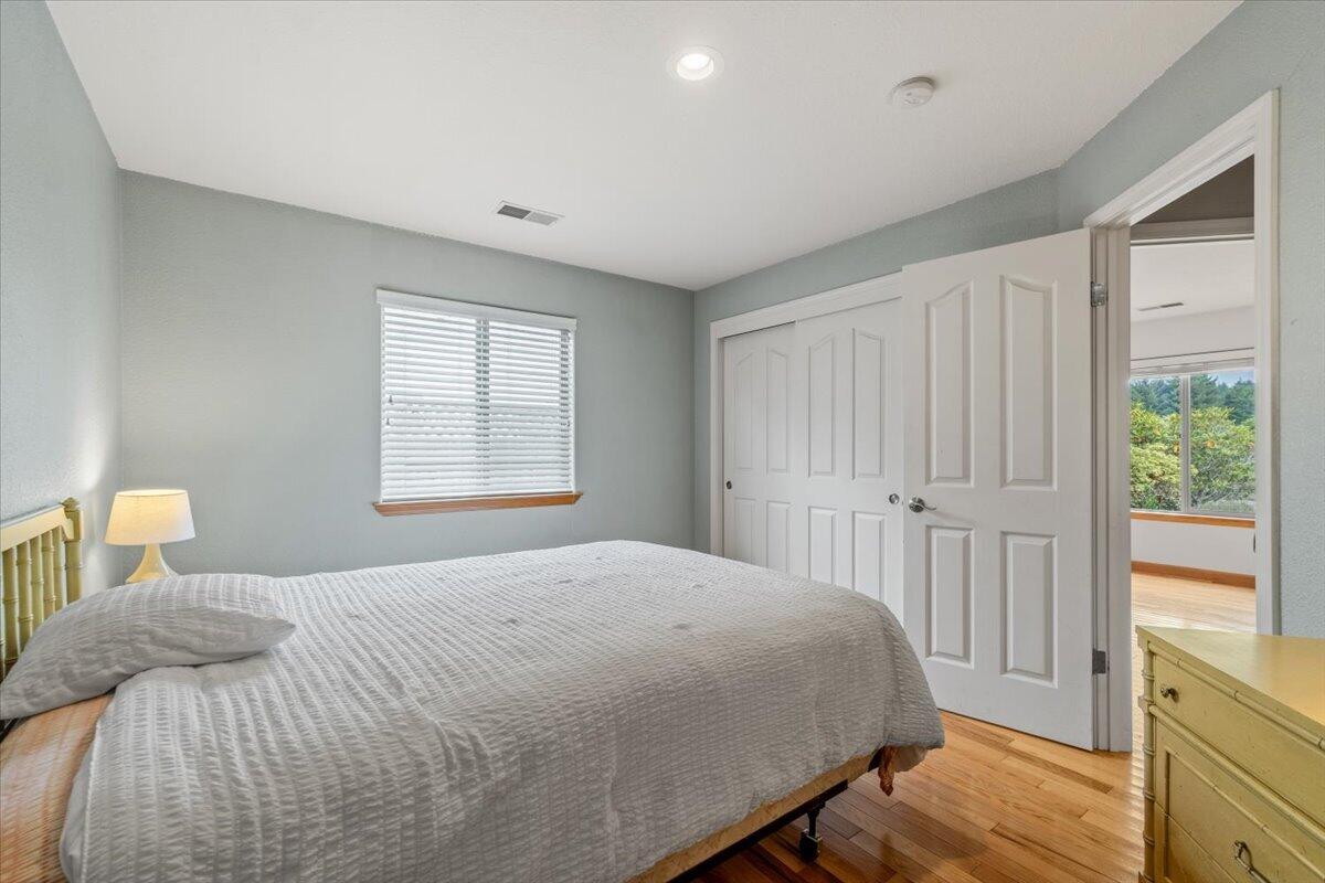 Bedroom with a gray quilted bed, open closet doors, and hardwood floors.